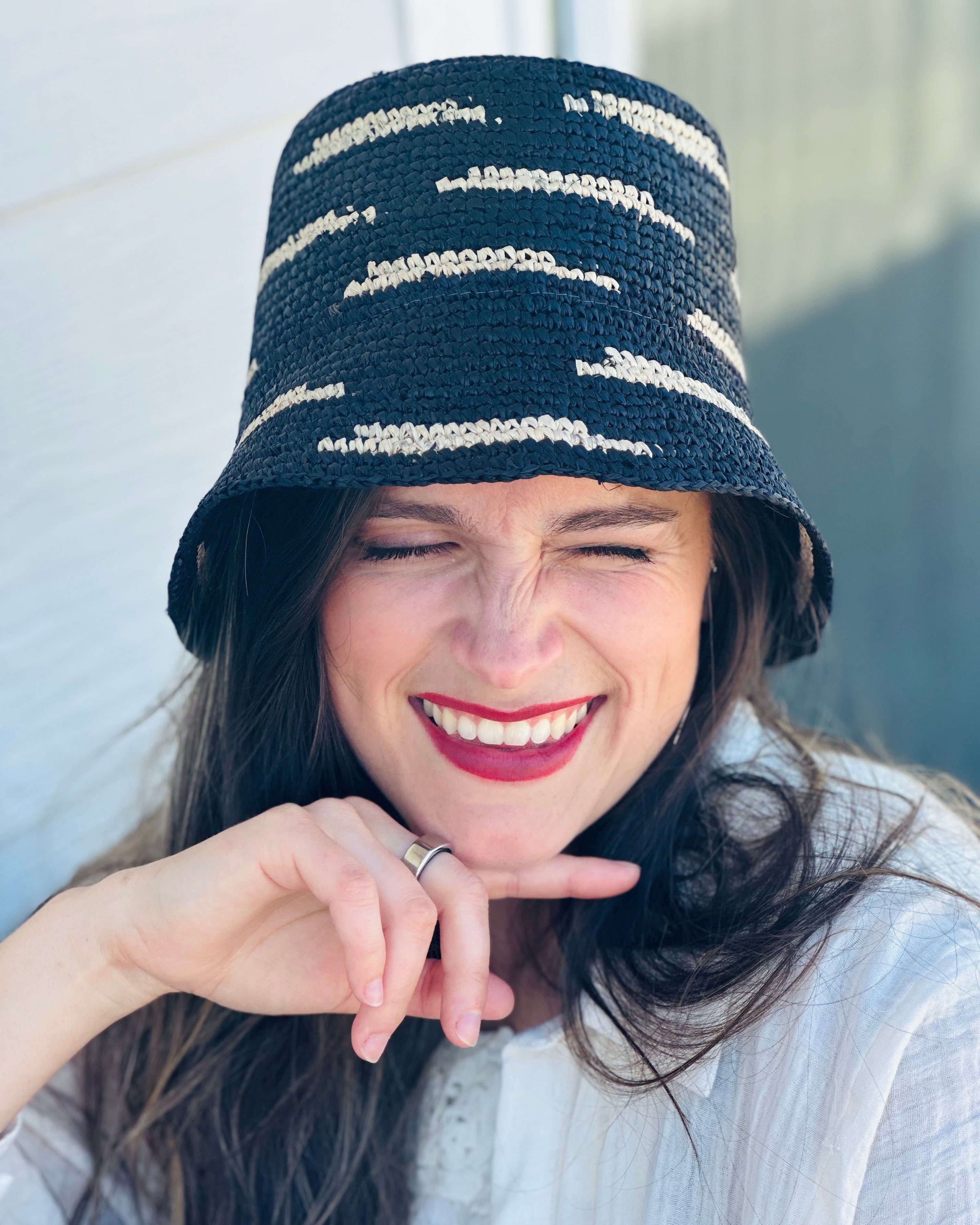 Model wearing 2.5" Brim Taylor Black Crochet Bucket Straw Hat with Zebra Stripes handmade raffia palm fiber in a two tone color combination of horizontal short stripes that create a dash pattern around the hat in black with natural straw color - Shebobo