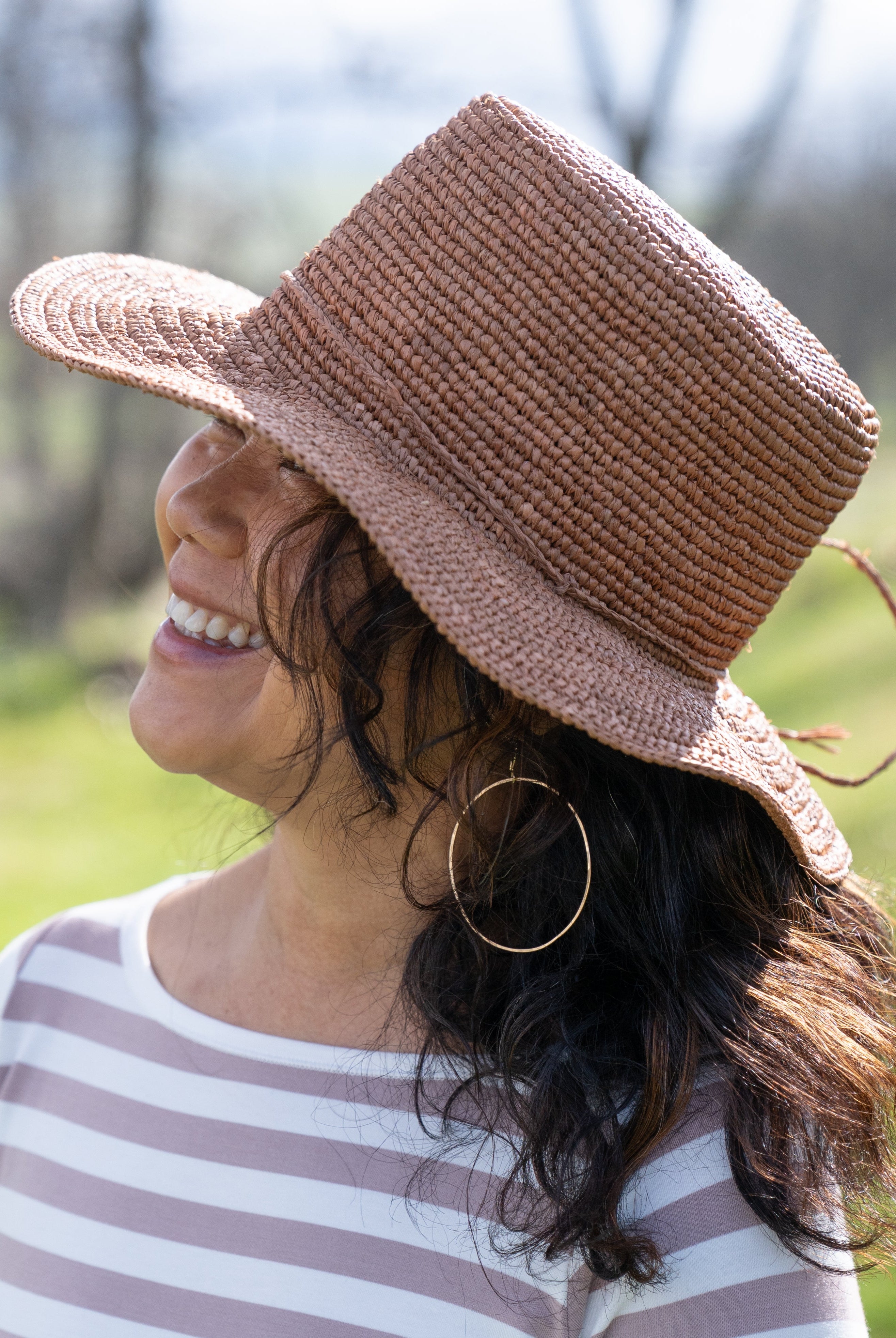 Model wearing 3" Brim Bolero Crochet Straw Sun Hats handmade crochet natural raffia palm fiber in a solid hue of cinnamon dark brown making a concentric pattern from the center top of the flattened crown spiraling out to the edge of the brim with matching adjustable raffia braid hat band - Shebobo