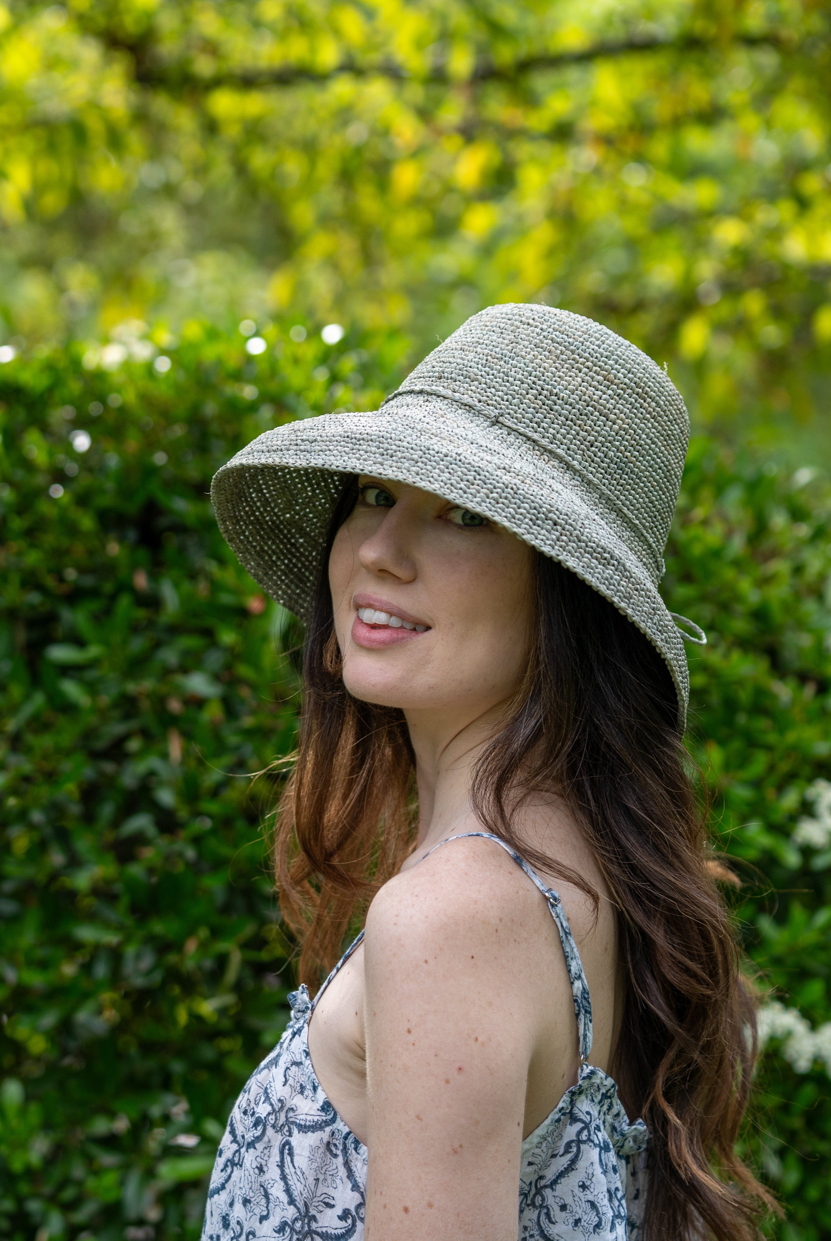 Model wearing Leor Ocean Mist crochet straw hat handmade woven natural raffia palm fiber in a solid hue of ocean mist/sage/pale/grey green color 3" brim packable straw hat with matching adjustable braided hat band - Shebobo