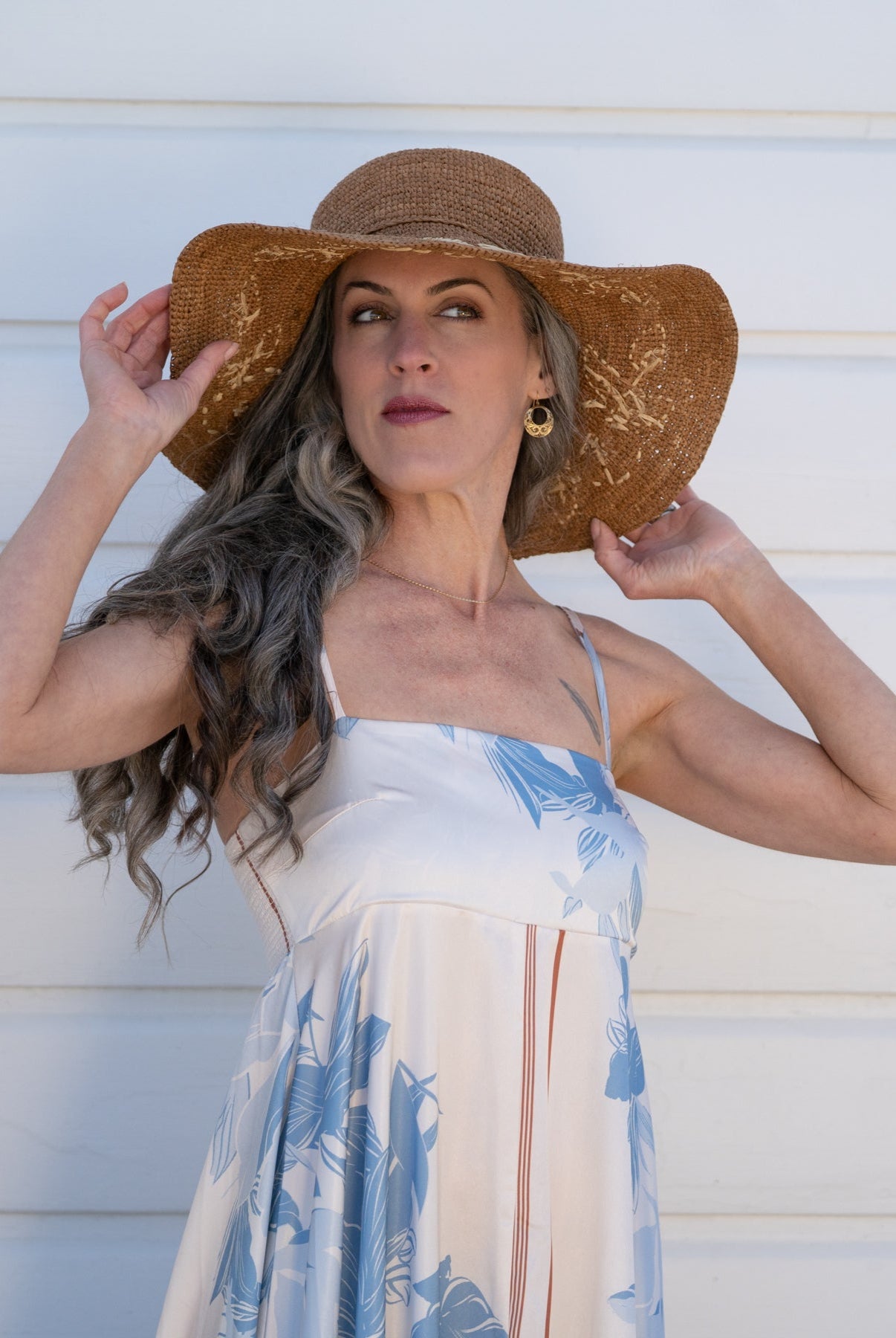 Model wearing 5.5" Brim Gigi Cinnamon and Natural Floral Embroidered Crochet Straw Sun Hats handmade crochet natural raffia palm fiber in a solid hue of cinnamon dark brown making a concentric pattern from the center top of the flattened crown spiraling out to the edge of the brim with matching adjustable raffia braid hat band and natural straw color floral pattern with leaves embroidered on the brim - Shebobo