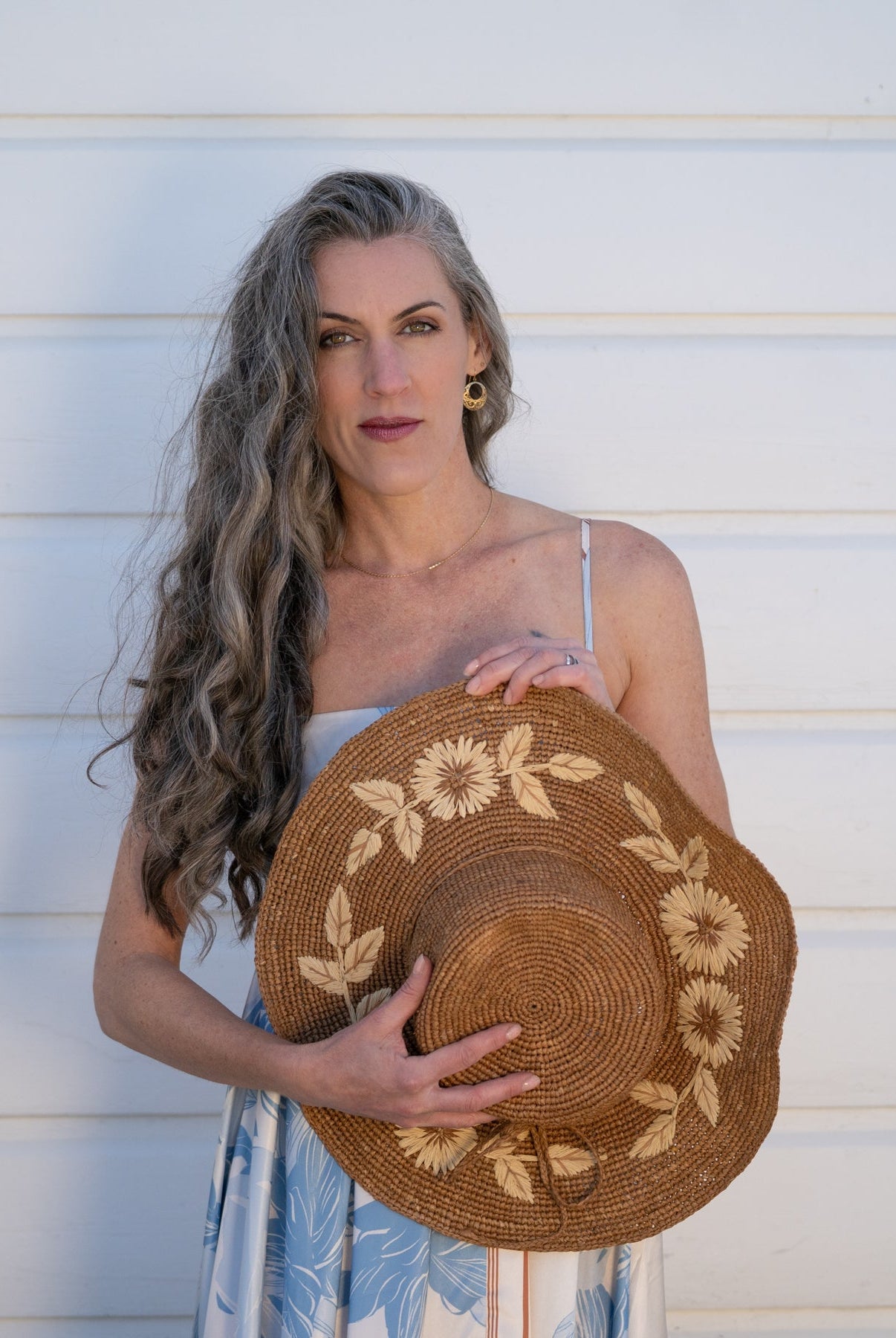 Model wearing 5.5" Brim Gigi Cinnamon and Natural Floral Embroidered Crochet Straw Sun Hats handmade crochet natural raffia palm fiber in a solid hue of cinnamon dark brown making a concentric pattern from the center top of the flattened crown spiraling out to the edge of the brim with matching adjustable raffia braid hat band and natural straw color floral pattern with leaves embroidered on the brim - Shebobo