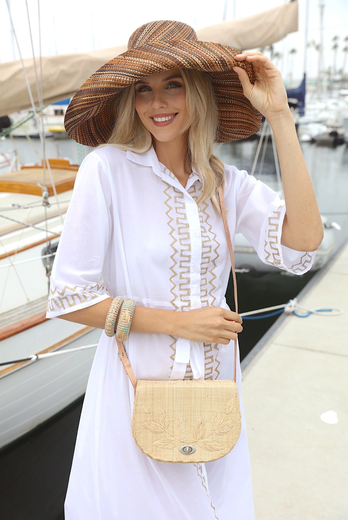 Model wearing 70's Crossbody Straw Bag handmade loomed natural raffia palm fiber purse with natural color accent cross stitch edging and matching leaf design embroidery handbag with adjustable leather strap - Shebobo