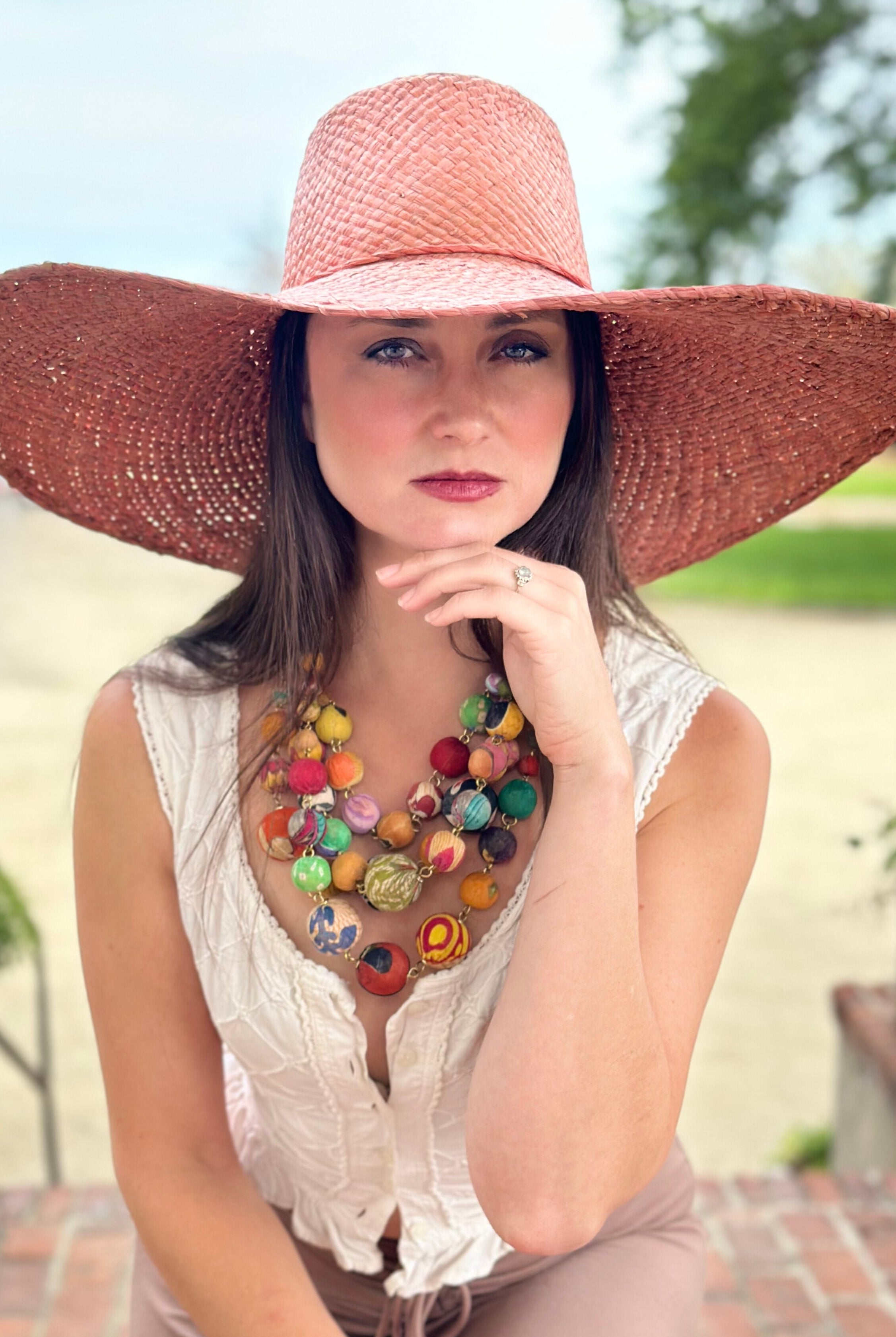 Model wearing 7" Wide Brim Natasha Rouge Woven XL Straw Sun Hat handmade woven natural raffia palm fiber in a solid hue of rouge red/pink with matching adjustable twisted raffia hat band and and extra wide brim - Shebobo