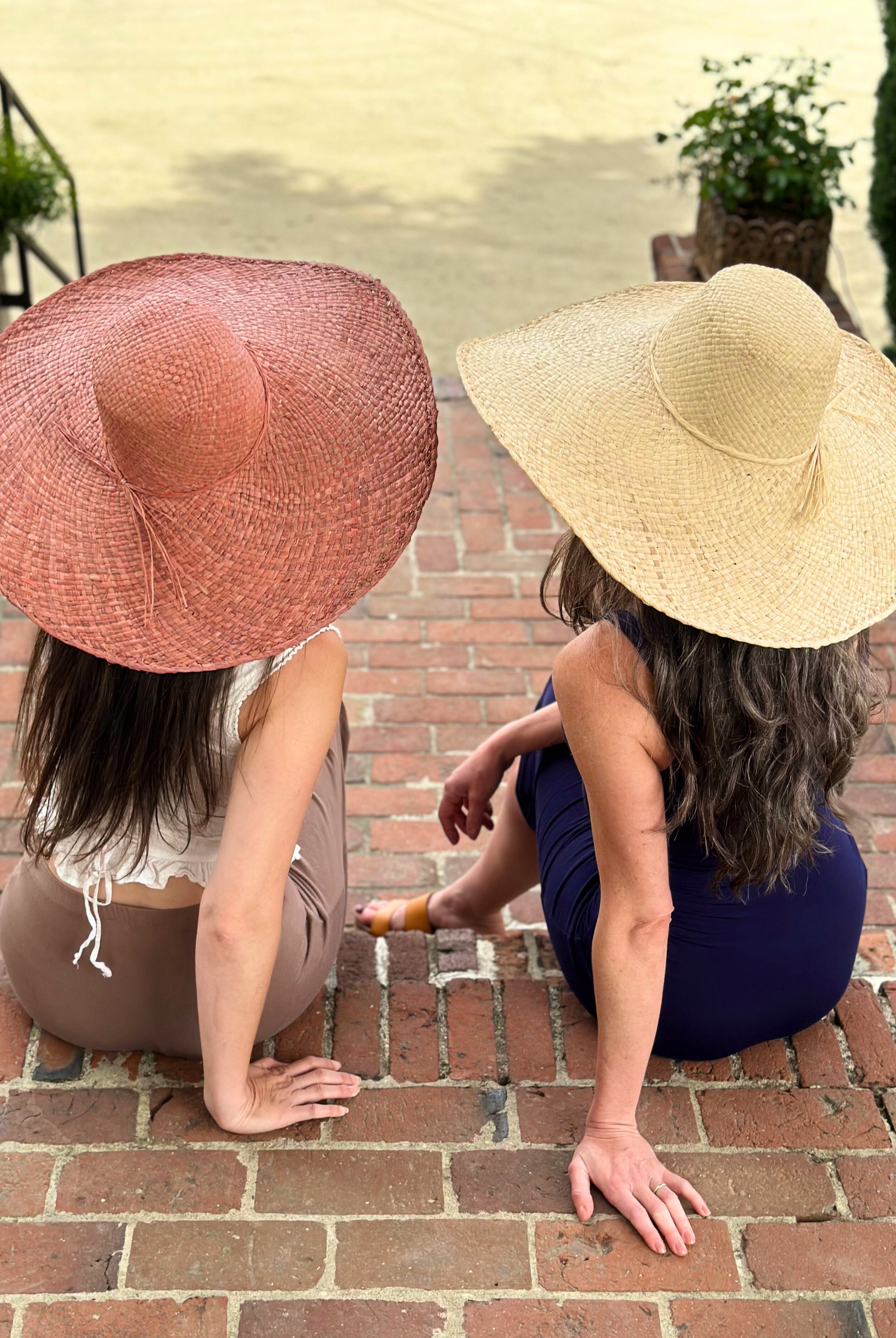 Model wearing 7" Wide Brim Natasha Natural Woven XL Straw Sun Hat handmade woven natural raffia palm fiber in a solid hue of straw color with matching adjustable twisted raffia hat band and and extra wide brim and the same hat in Rouge pink/red hue - Shebobo