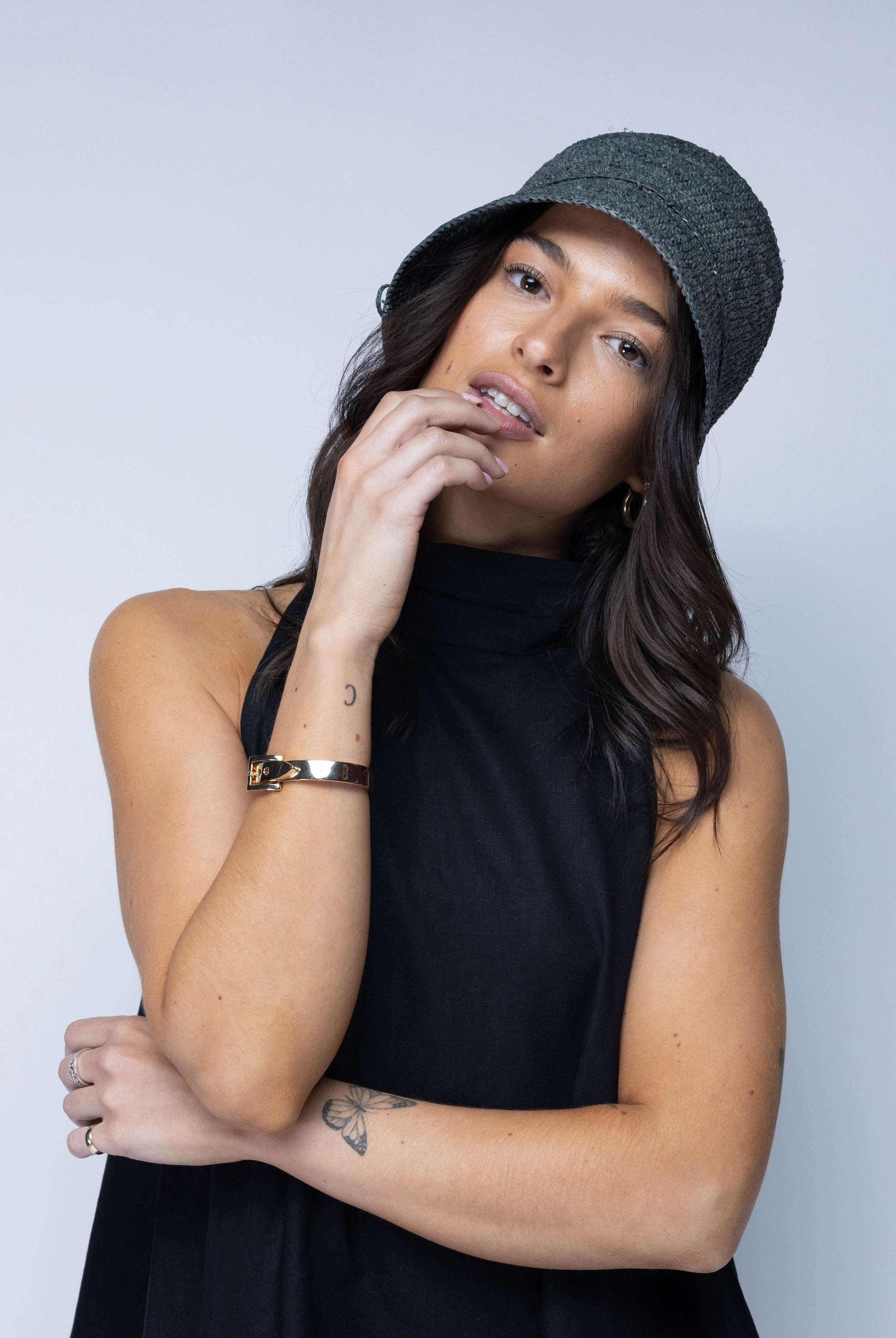 Model wearing Ali 2" Brim Crochet Bucket Raffia Straw Hats handmade natural raffia palm fiber in a subtle crochet link texture spiraling out from the top crown of the hat to the edge of the brim in a solid hue of gray with matching braided adjustable hat band sun hat - Shebobo