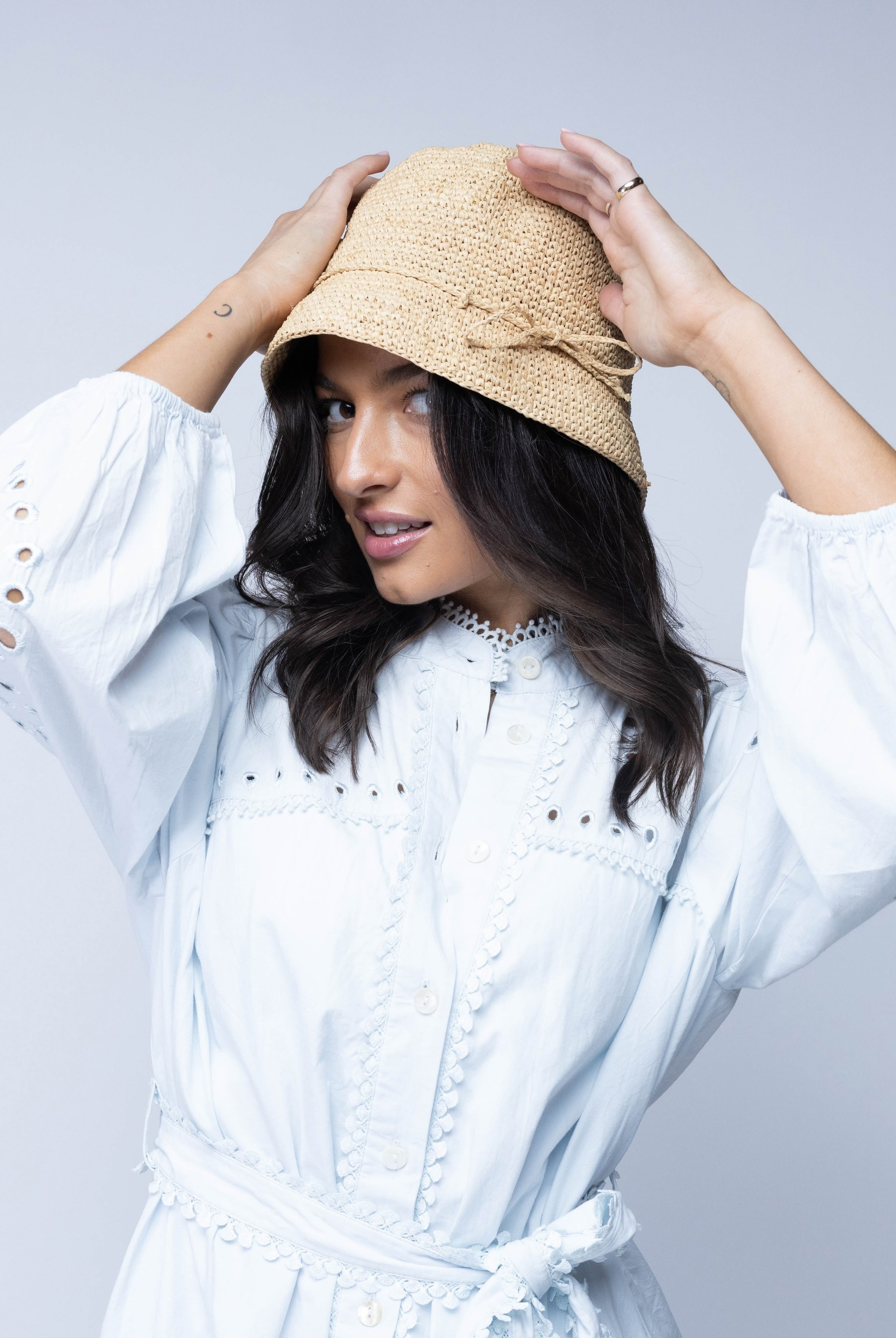 Model wearing Ali 2" Brim Crochet Bucket Raffia Straw Hats handmade natural raffia palm fiber in a subtle crochet link texture spiraling out from the top crown of the hat to the edge of the brim in a solid hue of natural straw color with matching braided adjustable hat band sun hat - Shebobo