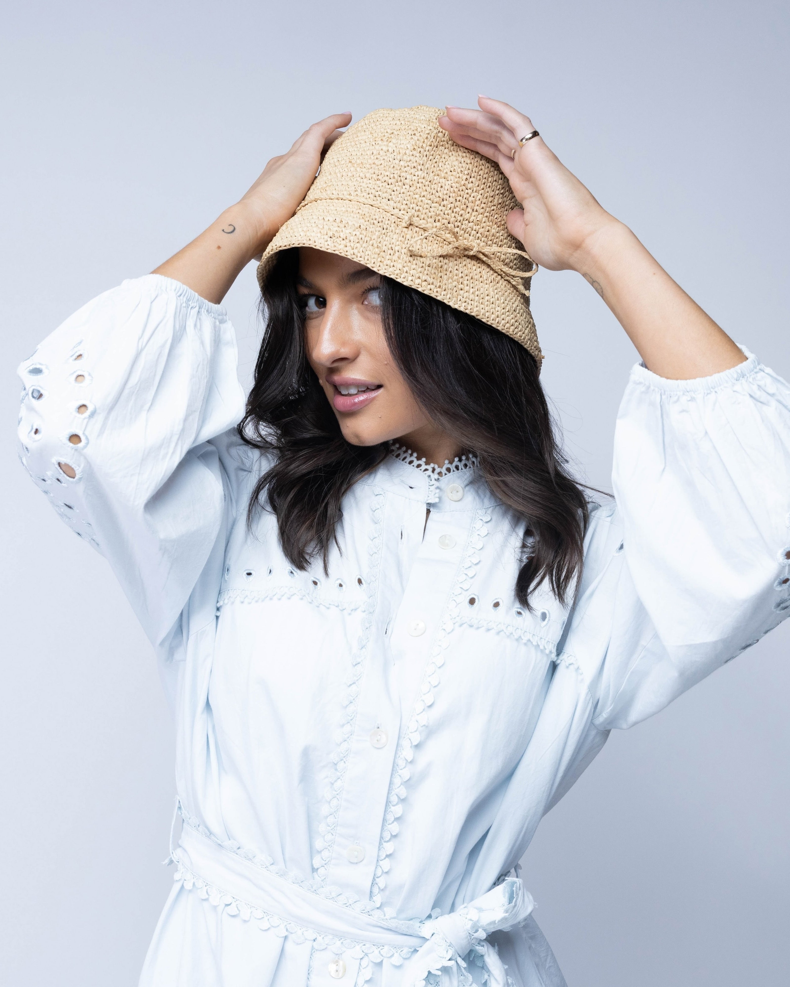 Model wearing Ali 2" Brim Crochet Bucket Raffia Straw Hats handmade natural raffia palm fiber in a subtle crochet link texture spiraling out from the top crown of the hat to the edge of the brim in a solid hue of natural straw color with matching braided adjustable hat band sun hat - Shebobo