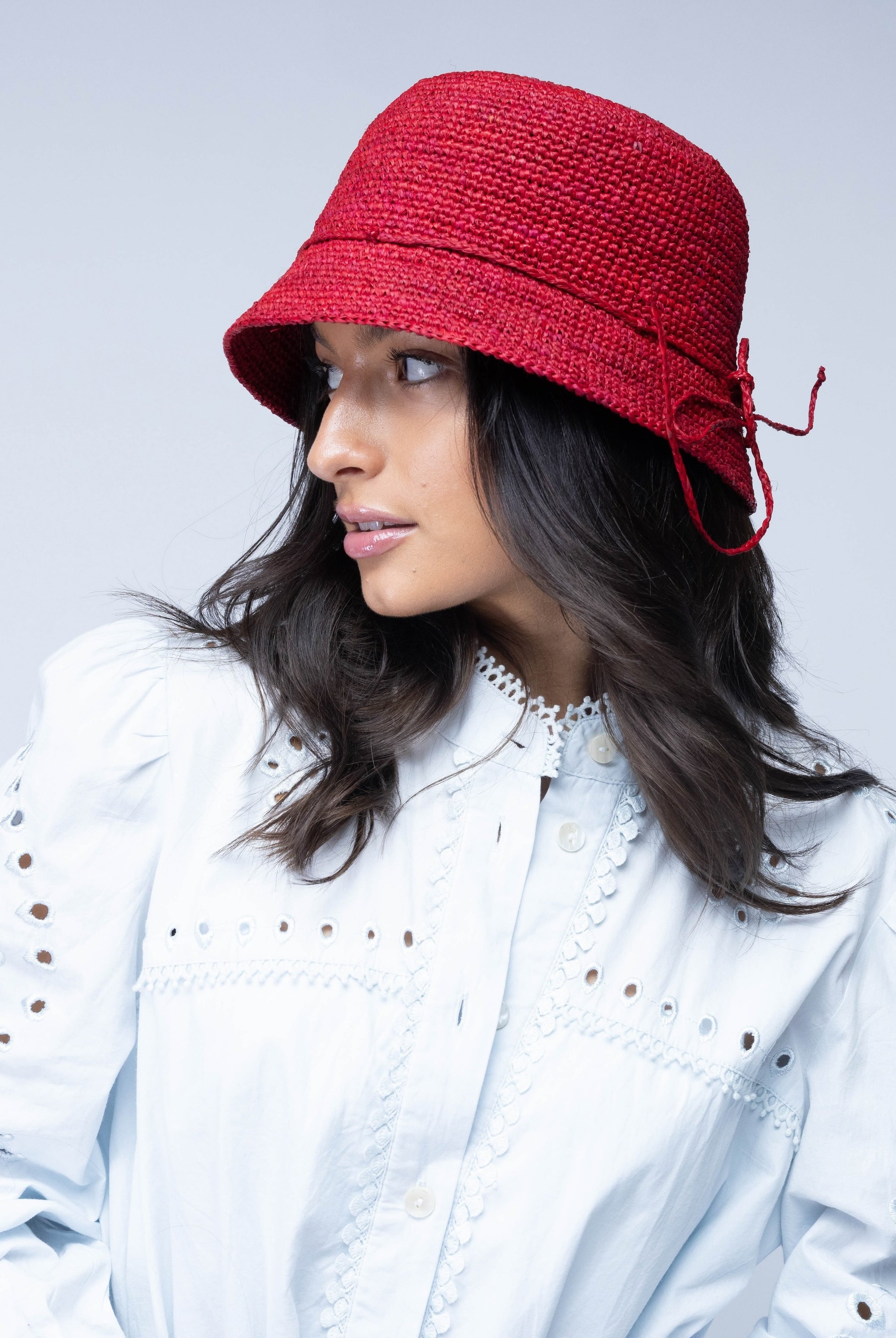 Model wearing Ali 2" Brim Crochet Bucket Raffia Straw Hats handmade natural raffia palm fiber in a subtle crochet link texture spiraling out from the top crown of the hat to the edge of the brim in a solid hue of red with matching braided adjustable hat band sun hat - Shebobo