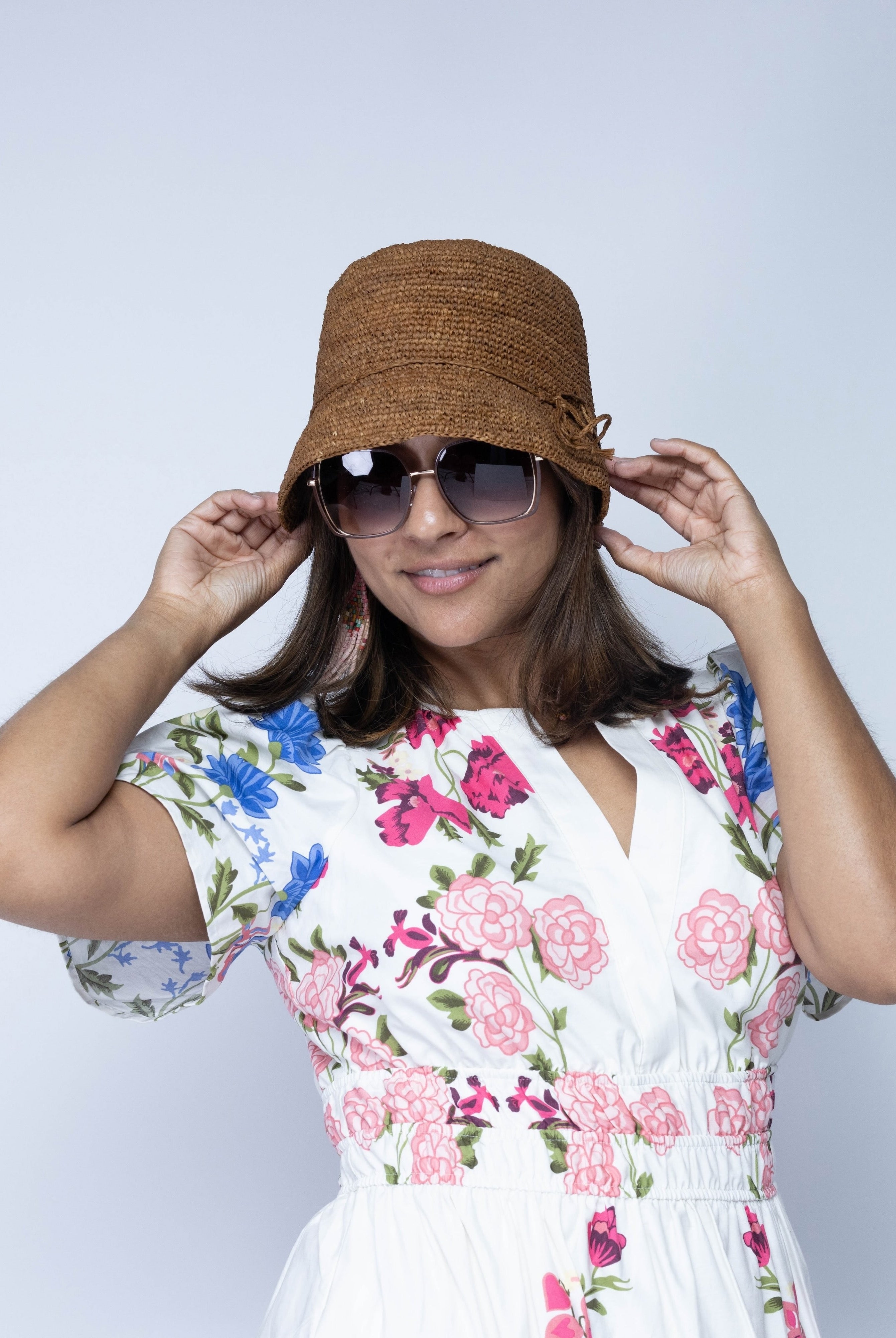 Model wearing Ali 2" Brim Crochet Bucket Raffia Straw Hats handmade natural raffia palm fiber in a subtle crochet link texture spiraling out from the top crown of the hat to the edge of the brim in a solid hue of tobacco cinnamon/dark/brown with matching braided adjustable hat band sun hat - Shebobo