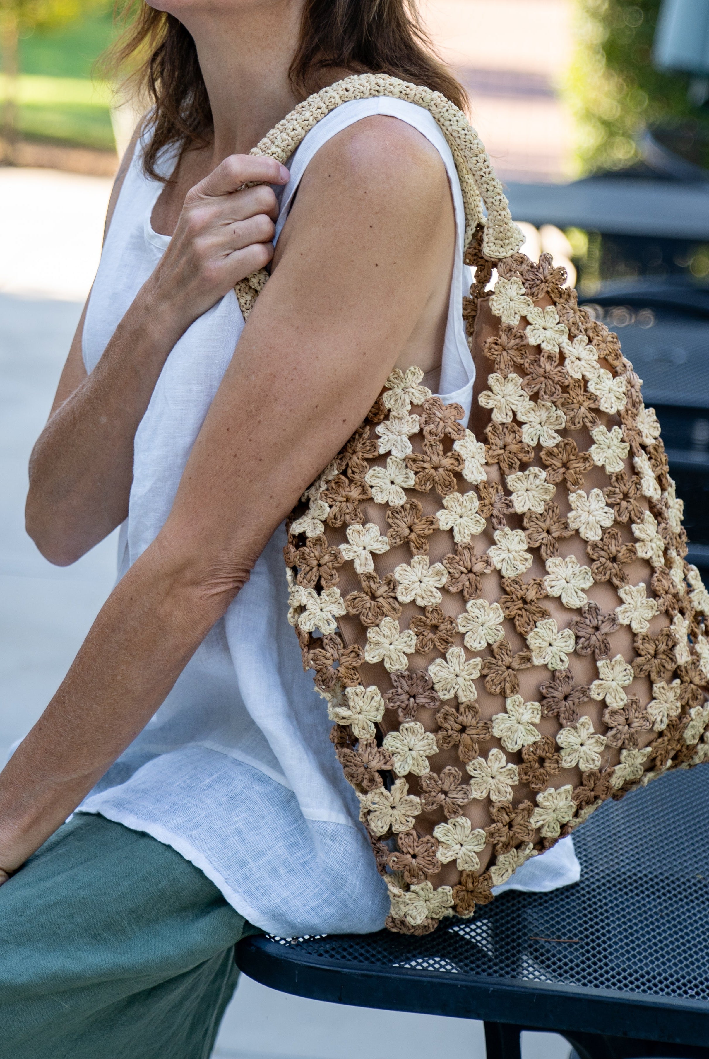 Model wearing Amalie Two Tone Daisy Flower Crochet Straw Handbag handmade crochet mini flower buds from crochet natural raffia palm fiber in an alternating colored pattern of cappuccino tea/light/brown and natural straw color with brown internal liner and natural woven handles purse - Shebobo