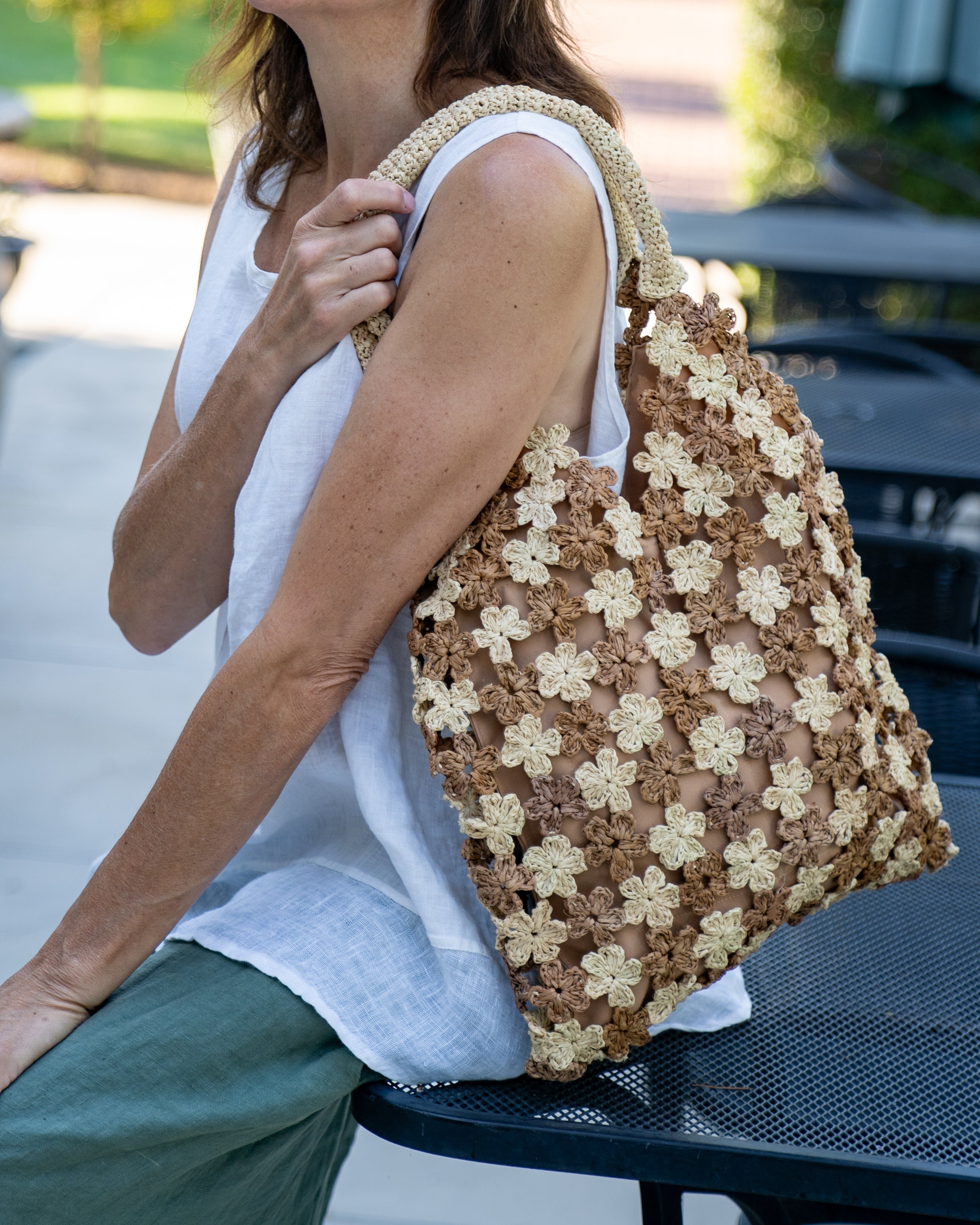 Model wearing Amalie Two Tone Daisy Flower Crochet Straw Handbag handmade crochet mini flower buds from crochet natural raffia palm fiber in an alternating colored pattern of cappuccino tea/light/brown and natural straw color with brown internal liner and natural woven handles purse - Shebobo