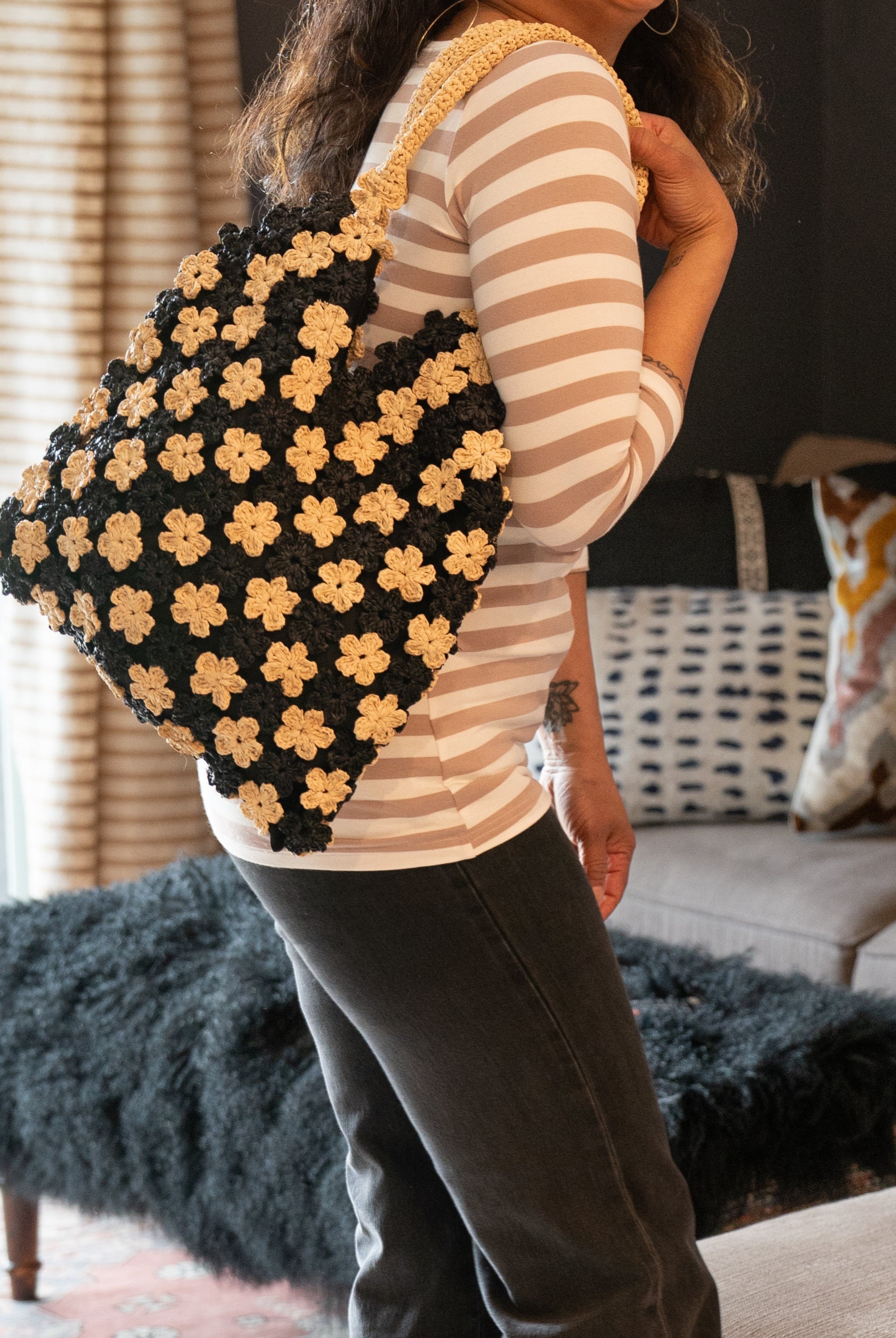 Model wearing Amalie Two Tone Daisy Flower Crochet Straw Handbag handmade crochet mini flower buds from crochet natural raffia palm fiber in an alternating colored pattern of black and natural straw color with black internal liner and natural woven handles purse - Shebobo