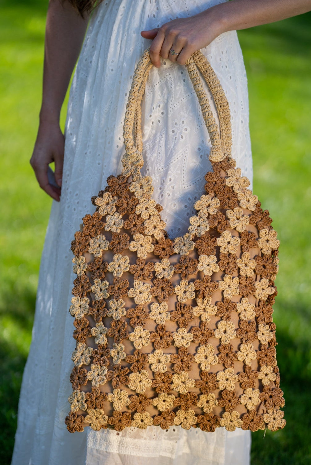 Model wearing Amalie Two Tone Daisy Flower Crochet Straw Handbag handmade crochet mini flower buds from crochet natural raffia palm fiber in an alternating colored pattern of cappuccino tea/light/brown and natural straw color with brown internal liner and natural woven handles purse - Shebobo
