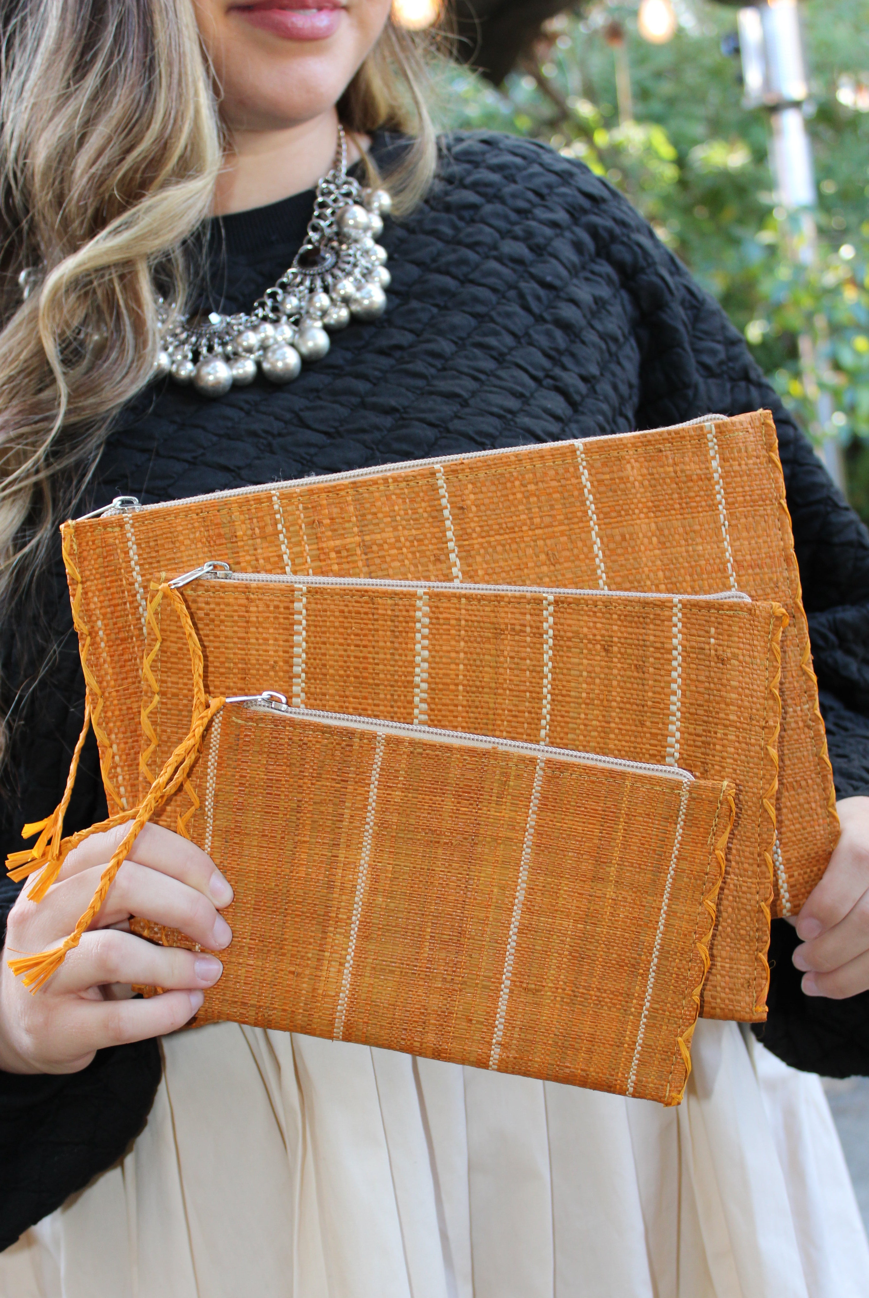 Model wearing Amelia Set of 3 Saffron Nesting Zippered Straw Clutches Pinstripe Pattern handmade loomed raffia in wide vertical bands of saffron yellow with narrow bands of natural straw color with matching zipper and braided zipper pull with cross stitch edging in three sizes of small, medium, and large - Shebobo