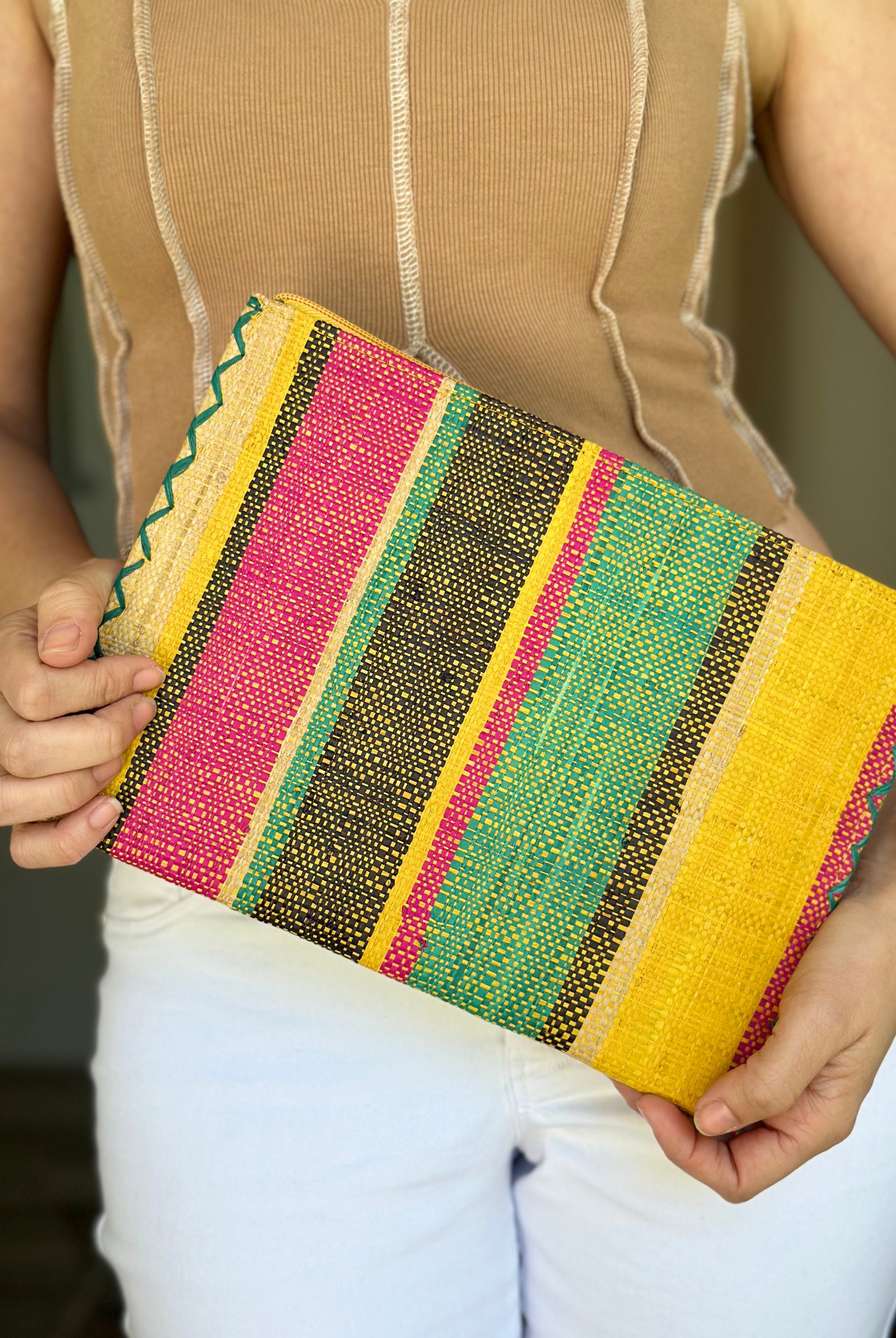 Model wearing Amelia Set of 3 Nesting Zippered Straw Clutches Carmalita Multicolor Stripe Pattern handmade loomed raffia in multiple widths of vertical stripes in turquoise, black, fuchsia, and saffron with matching zipper and braided zipper pull with cross stitch edging in three sizes of small, medium, and large - Shebobo