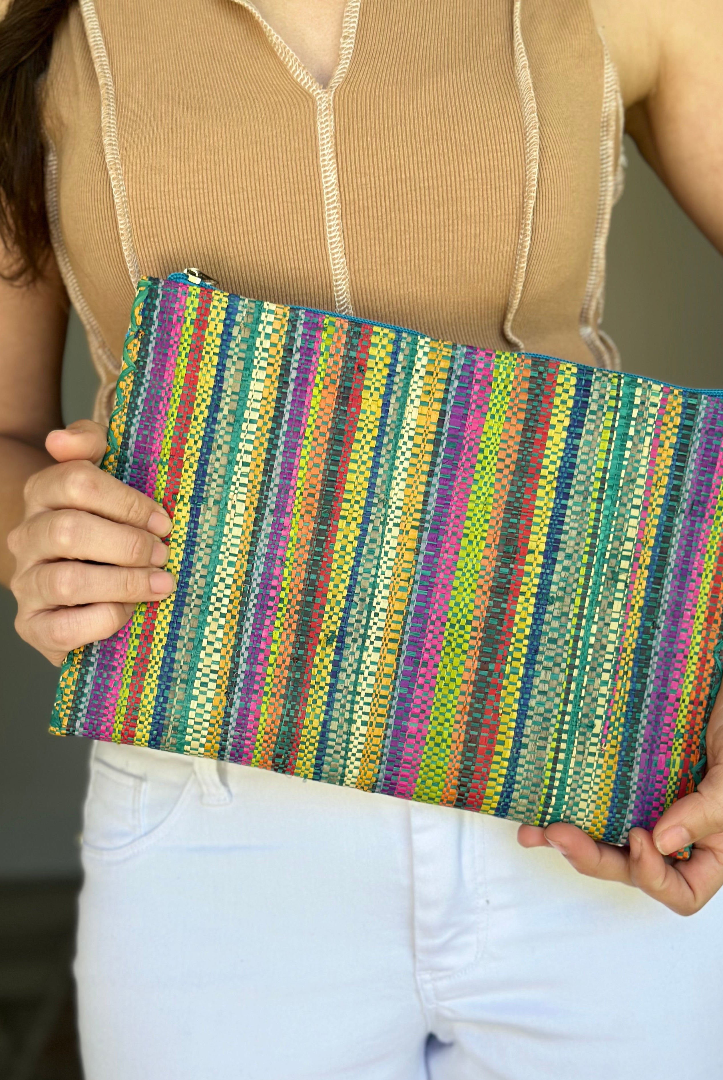 Model wearing Amelia Set of 3 Nesting Zippered Straw Clutches Turquoise Stripe Multicolor Stripe Pattern handmade loomed raffia in multiple widths of vertical stripes in natural, orange, turquoise, saffron, seafoam, red, fuchsia pink, etc. with matching turquoise zipper and braided zipper pull with cross stitch edging in three sizes of small, medium, and large - Shebobo