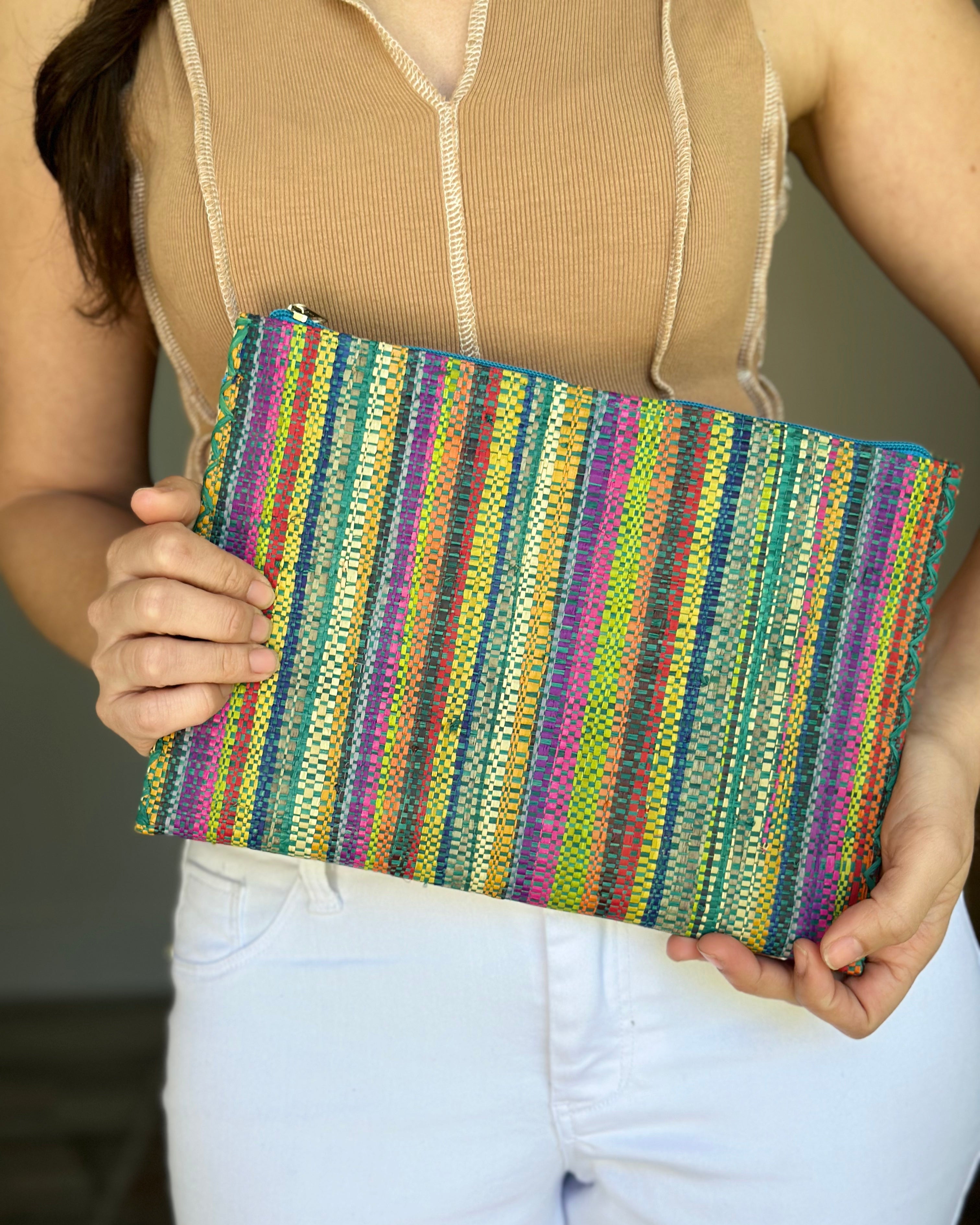 Model wearing Amelia Set of 3 Nesting Zippered Straw Clutches Turquoise Stripe Multicolor Stripe Pattern handmade loomed raffia in multiple widths of vertical stripes in natural, orange, turquoise, saffron, seafoam, red, fuchsia pink, etc. with matching turquoise zipper and braided zipper pull with cross stitch edging in three sizes of small, medium, and large - Shebobo