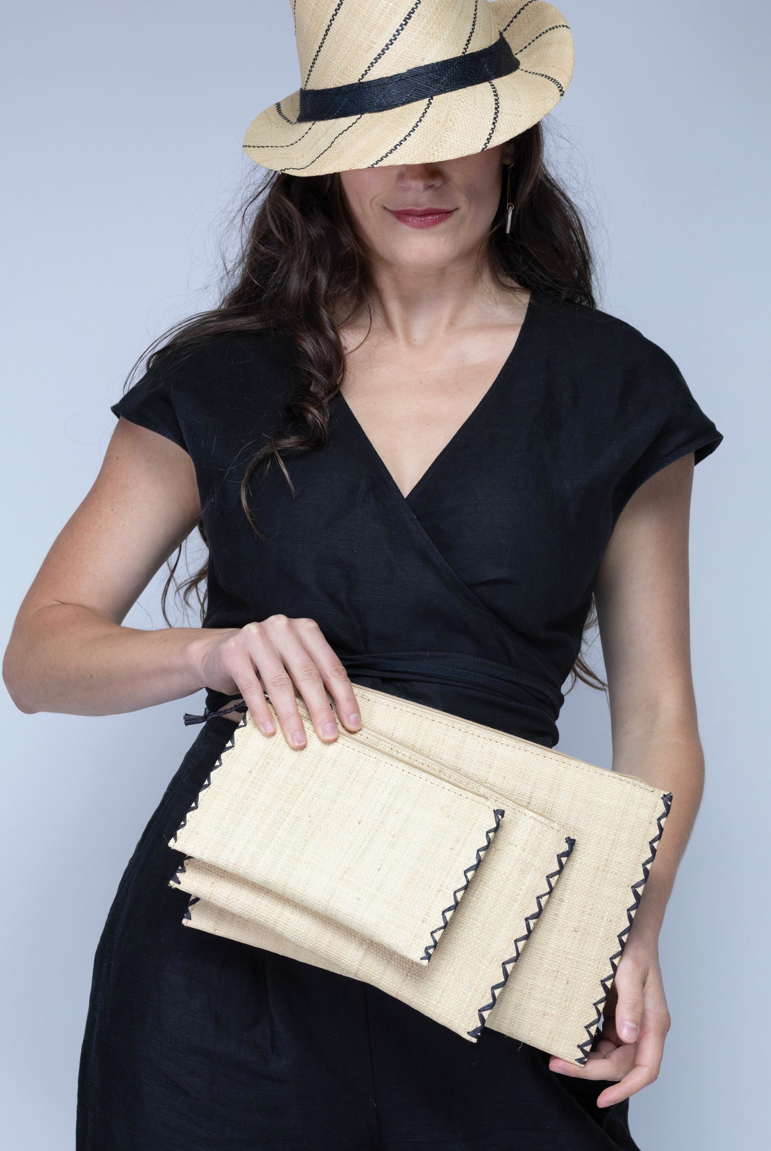 Model wearing Amelia Set of 3 Natural straw color Nesting Zippered Straw Clutches Solid Colors handmade loomed raffia in a solid hue with matching zipper and braided zipper pull with cross stitch edging in three sizes of small, medium, and large - Shebobo (with Fedra Fedora Unisex Straw Sun Hat)