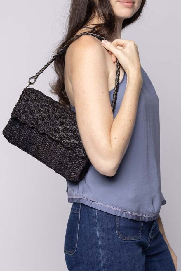 Model wearing Anna Petal Pattern Crochet Straw Over Shoulder Envelope Clutch Purse handmade raffia palm fiber in a solid hue of Black crochet in multiple textures resulting in a subtle pattern of vertical linked bands on the bottom half of the bag, and a floral petal or shell pattern on the upper envelope flap with braided leather shoulder strap handbag shoulder bag - Shebobo