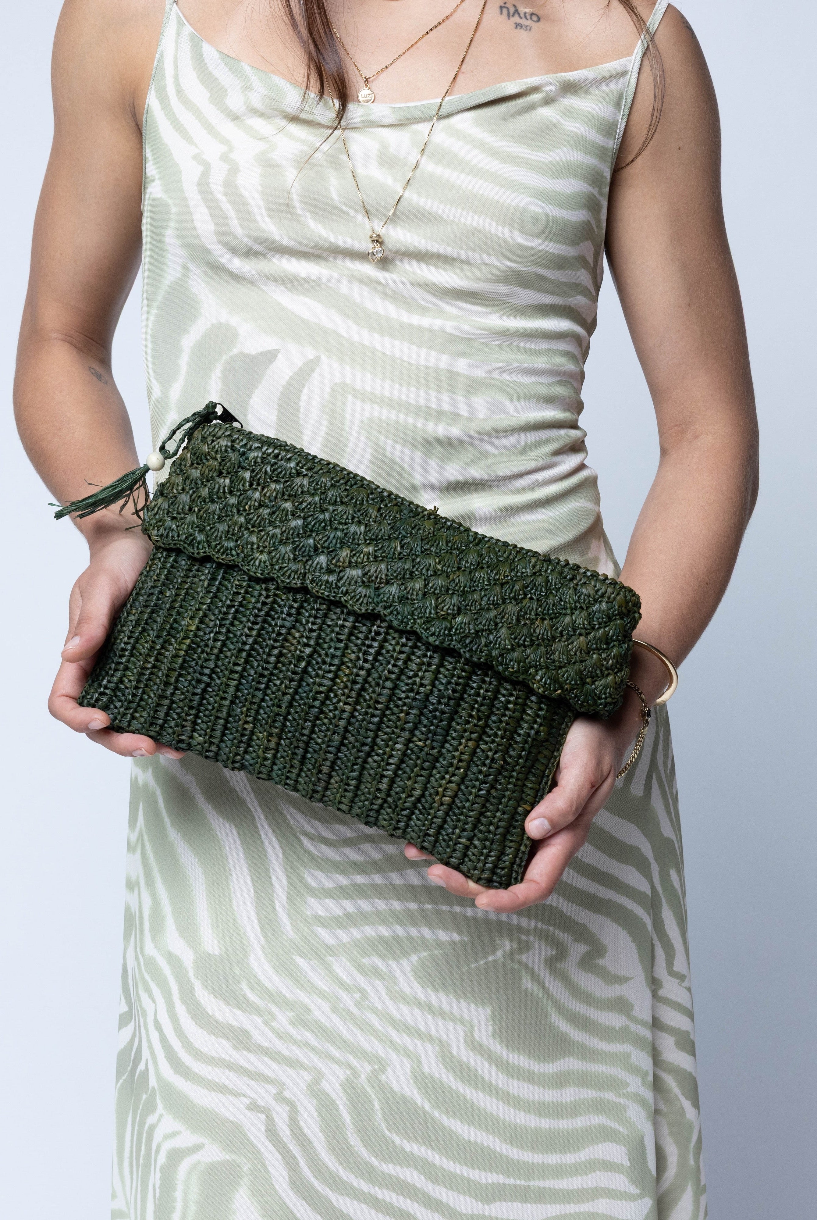 Model wearing Anna Petal Pattern Crochet Straw Pouch Clutch Purse handmade natural raffia palm fiber in a solid hue of Deep Green dark/forrest/green crochet in multiple textures resulting in a subtle pattern of vertical linked bands on the bottom half of the bag, and a floral petal or shell pattern on the upper half - Shebobo