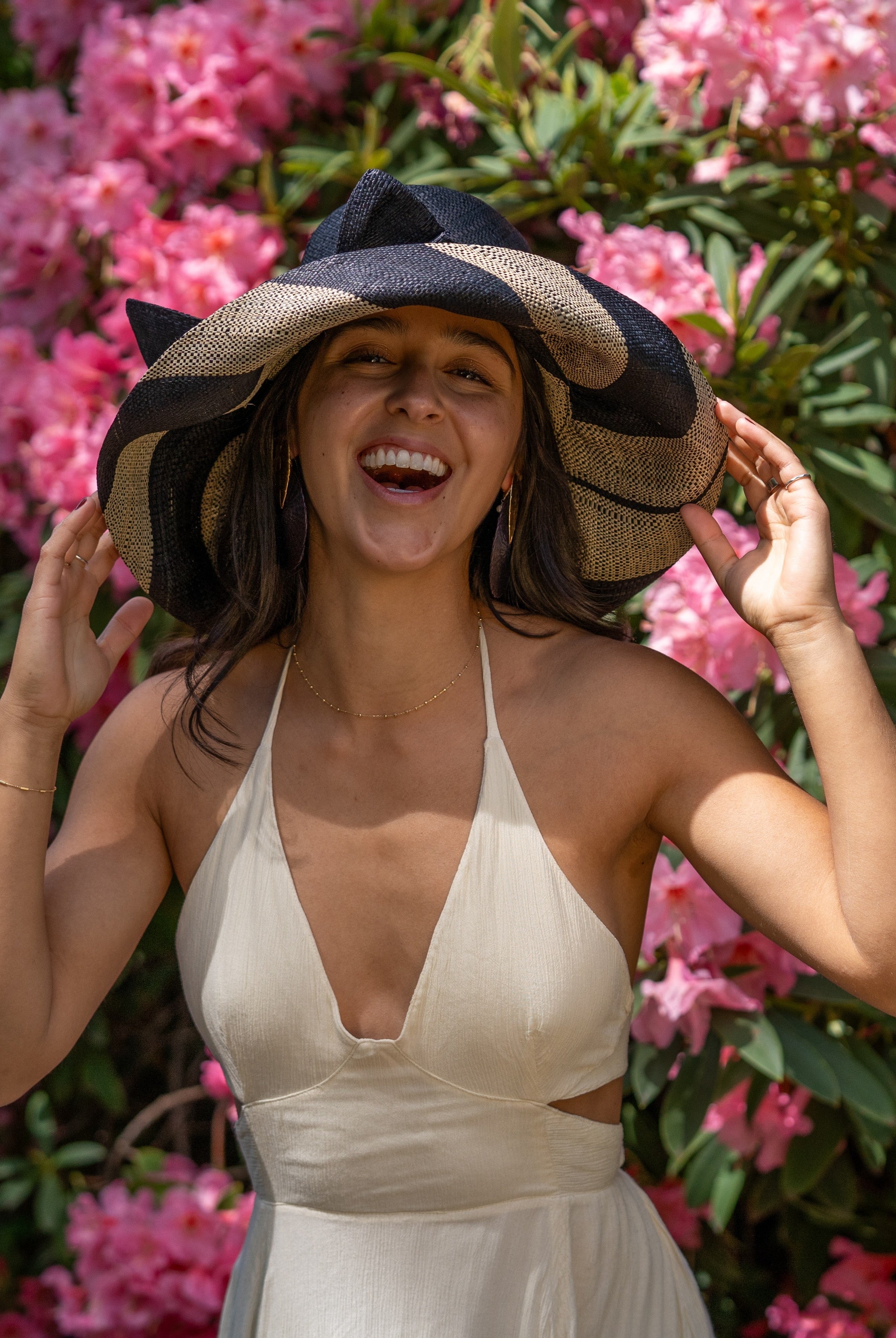 Model wearing Audrey 5" Wide Brim Black Two Tone Wide Stripe Straw Sun Hats with Big Bow handmade loomed raffia palm fiber in a solid hue of Black on the crown and matching oversized big bow embellishment hat band, with two tone even width wide stripe pattern of black and natural straw color that creates a swirl patterned brim - Shebobo