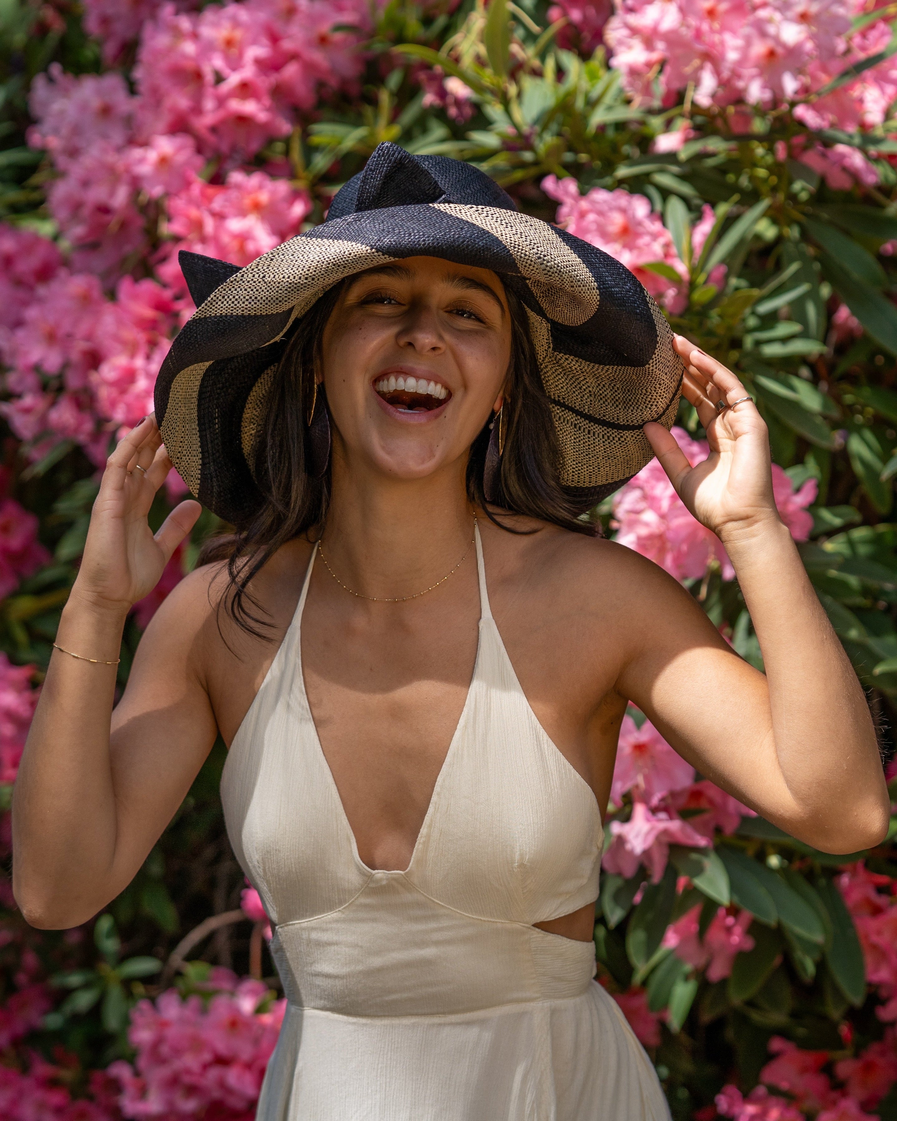 Model wearing Audrey 5" Wide Brim Black Two Tone Wide Stripe Straw Sun Hats with Big Bow handmade loomed raffia palm fiber in a solid hue of Black on the crown and matching oversized big bow embellishment hat band, with two tone even width wide stripe pattern of black and natural straw color that creates a swirl patterned brim - Shebobo