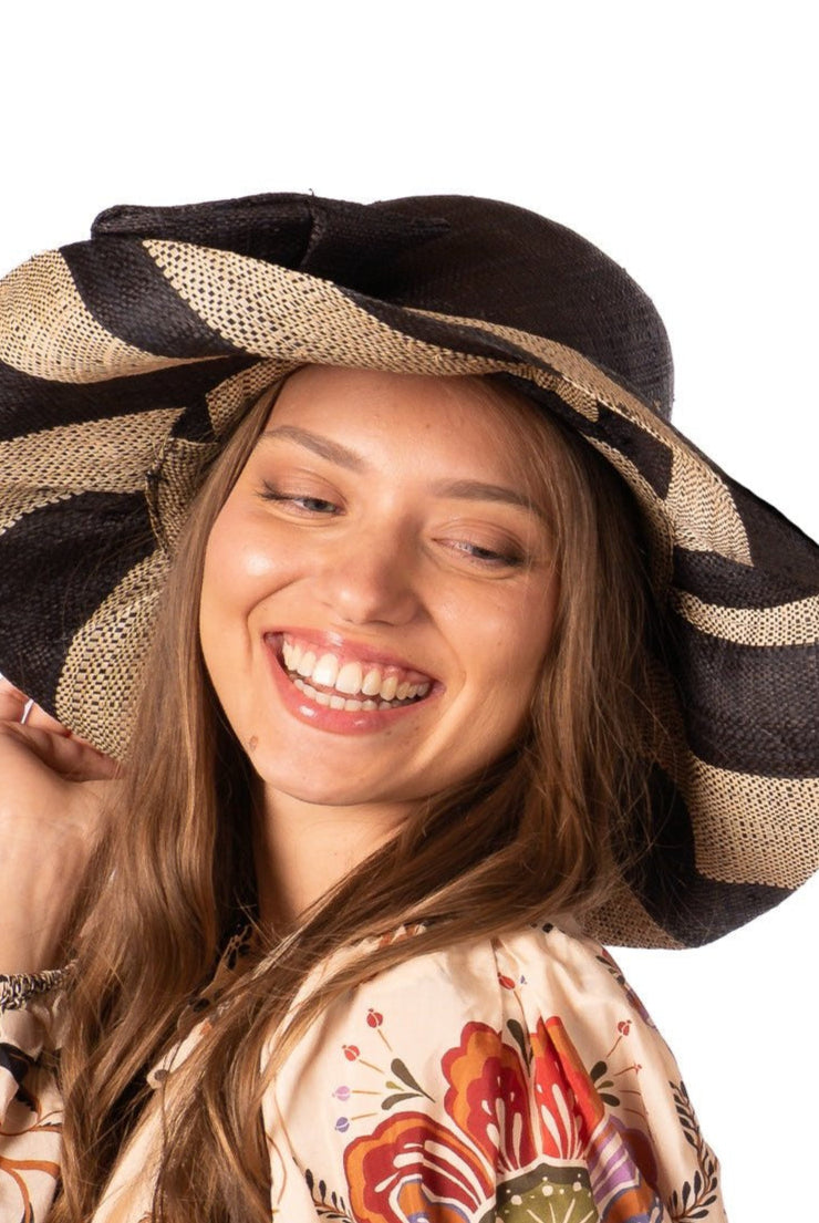 Model wearing Audrey 5" Wide Brim Black Two Tone Wide Stripe Straw Sun Hats with Big Bow handmade loomed raffia palm fiber in a solid hue of Black on the crown and matching oversized big bow embellishment hat band, with two tone even width wide stripe pattern of black and natural straw color that creates a swirl patterned brim - Shebobo
