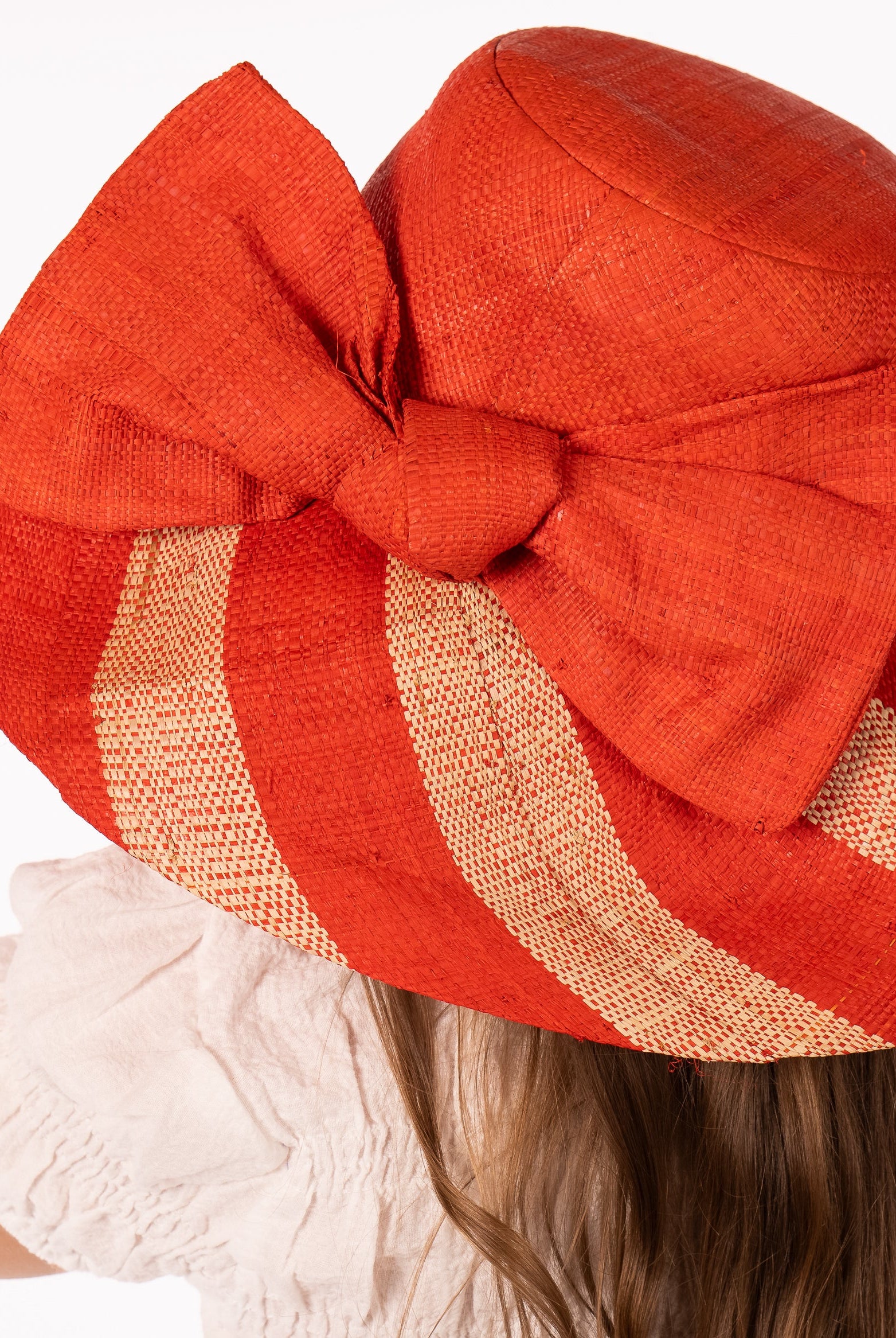Model wearing Audrey 5" Wide Brim Coral Two Tone Wide Stripe Straw Sun Hats with Big Bow handmade loomed raffia palm fiber in a solid hue of Coral orange/red on the crown and matching oversized big bow embellishment hat band, with two tone even width wide stripe pattern of coral and natural straw color that creates a swirl patterned brim - Shebobo