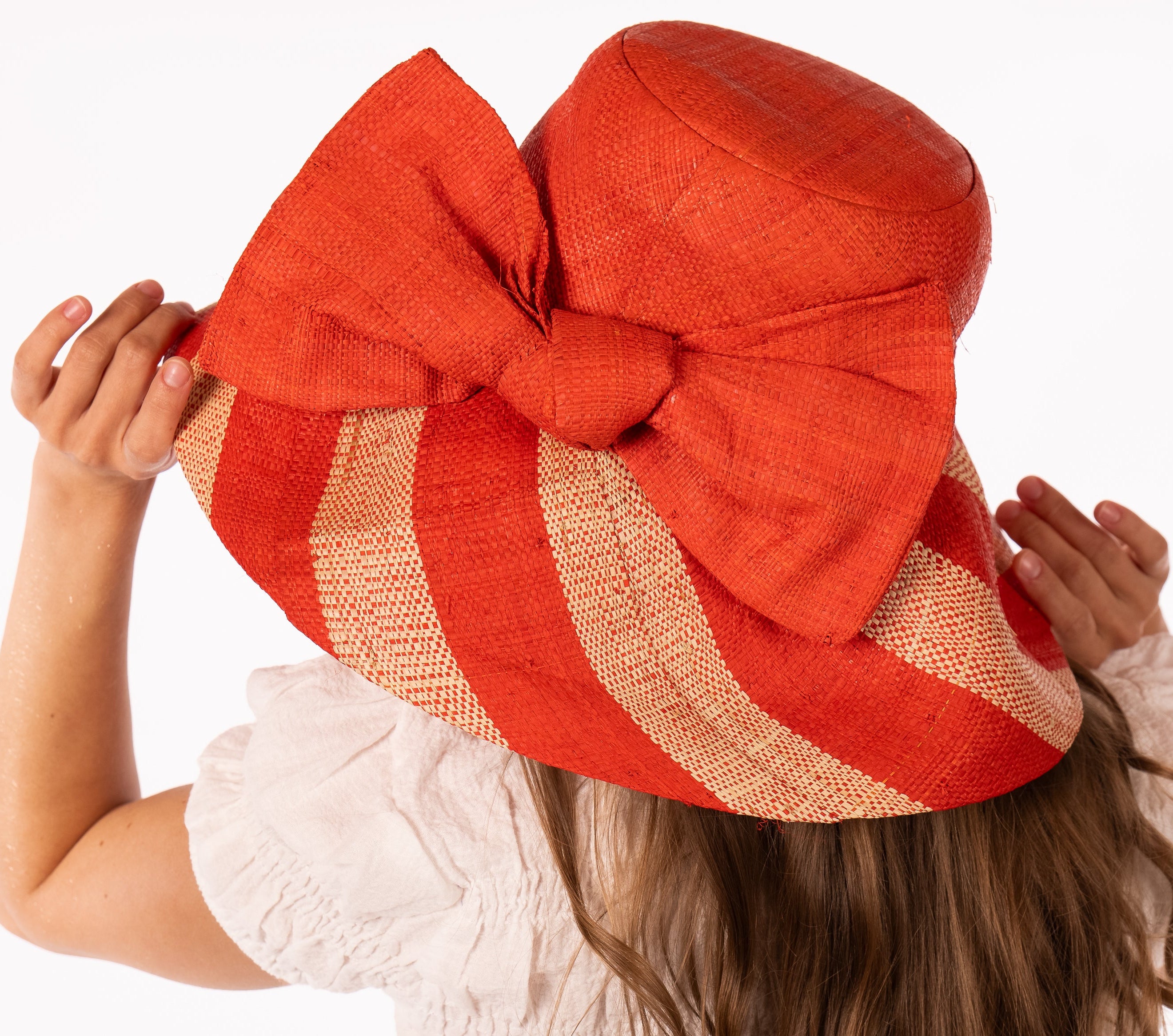 Model wearing Audrey 5" Wide Brim Coral Two Tone Wide Stripe Straw Sun Hats with Big Bow handmade loomed raffia palm fiber in a solid hue of Coral orange/red on the crown and matching oversized big bow embellishment hat band, with two tone even width wide stripe pattern of coral and natural straw color that creates a swirl patterned brim - Shebobo