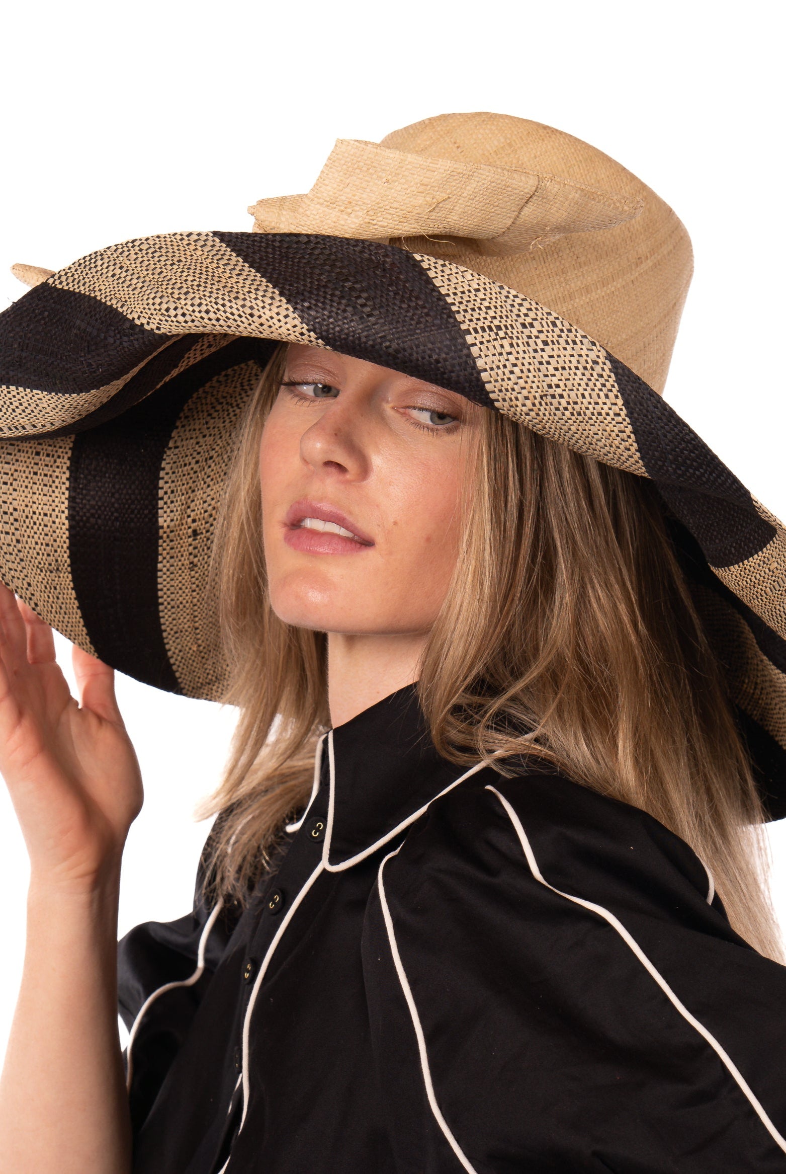 Model wearing Audrey 7" Wide Brim Natural Two Tone Wide Stripe Straw Sun Hats with Big Bow handmade loomed raffia palm fiber in a solid hue of Natural on the crown and matching oversized big bow embellishment hat band, with two tone even width wide stripe pattern of black and natural straw color that creates a swirl patterned brim - Shebobo