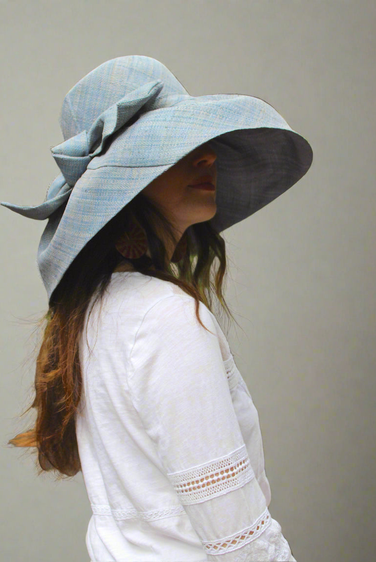 Model wearing Audrey 7" Wide Brim Solid Color Straw Sun Hats with Big Bow handmade loomed natural raffia straw fiber in a solid hue of Denim retro/light/blue with matching oversized big bow embellishment hat band - Shebobo