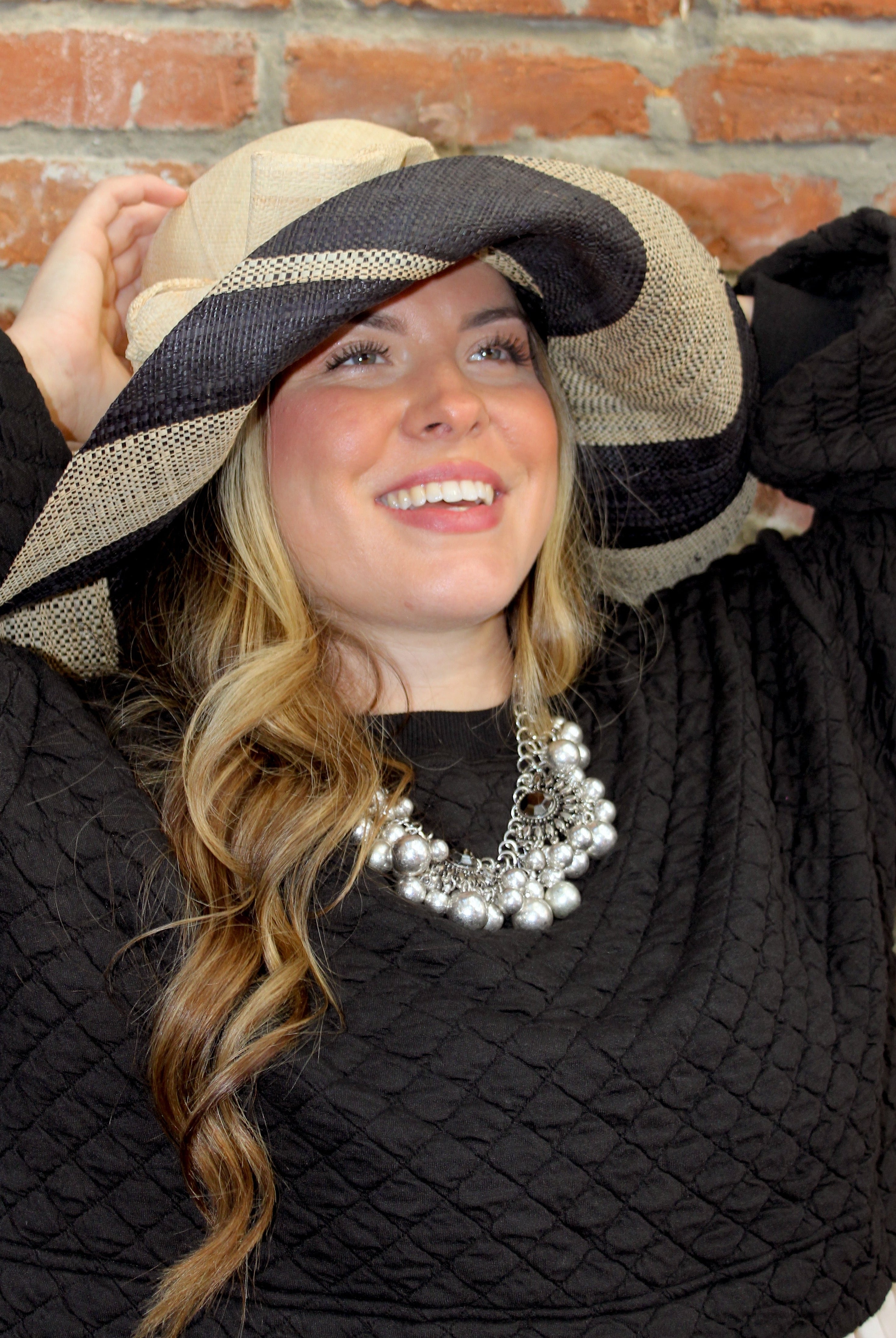 Model wearing Audrey 5" Wide Brim Natural Two Tone Wide Stripe Straw Sun Hats with Big Bow handmade loomed raffia palm fiber in a solid hue of Natural on the crown and matching oversized big bow embellishment hat band, with two tone even width wide stripe pattern of black and natural straw color that creates a swirl patterned brim - Shebobo
