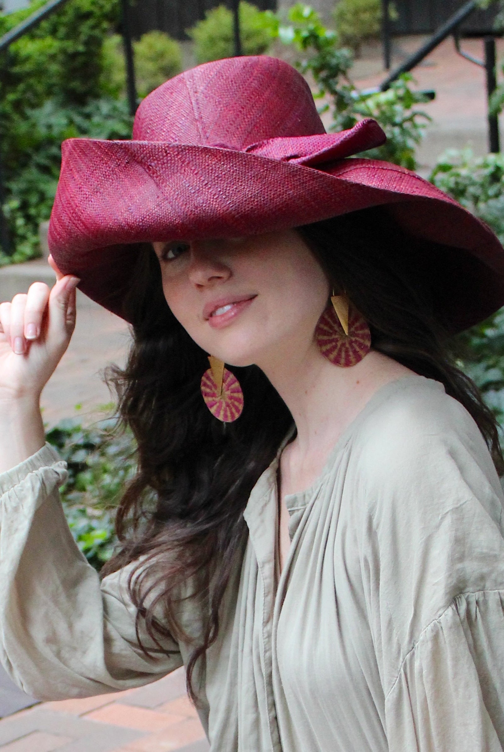 Model wearing Audrey 7" Wide Brim Solid Color Straw Sun Hats with Big Bow handmade loomed natural raffia straw fiber in a solid hue of Umberwine bordeaux/claret/deep/dark/red/purple with matching oversized big bow embellishment hat band - Shebobo