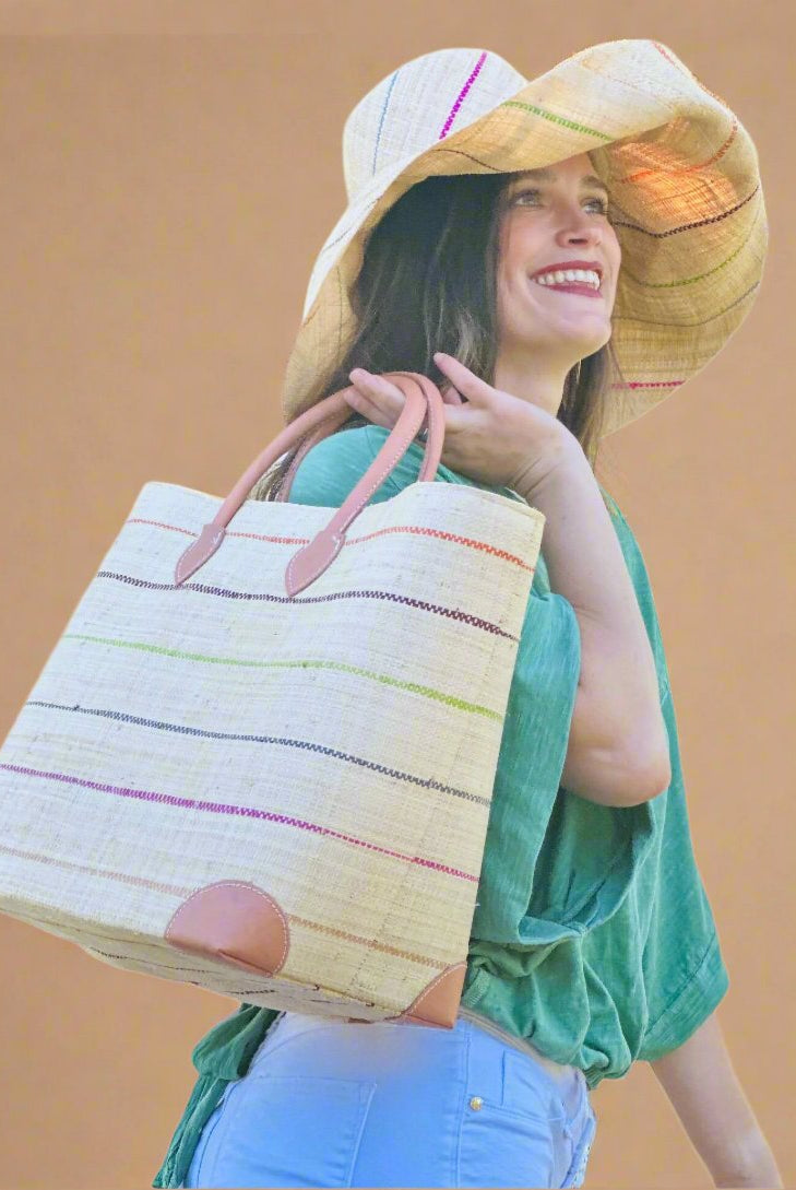 Model wearing Augustine pinstripes straw basket bag handmade loomed raffia in natural wide horizontal bands with multicolor bright colors of coral red/orange, bordeaux dark red, lime, grey, and fuchsia pink small bands running through in a stripe pattern with leather accents and handles handbag purse with Monica 7" Packable Brights Multicolor Pinstripe Straw Sun Hat - Shebobo
