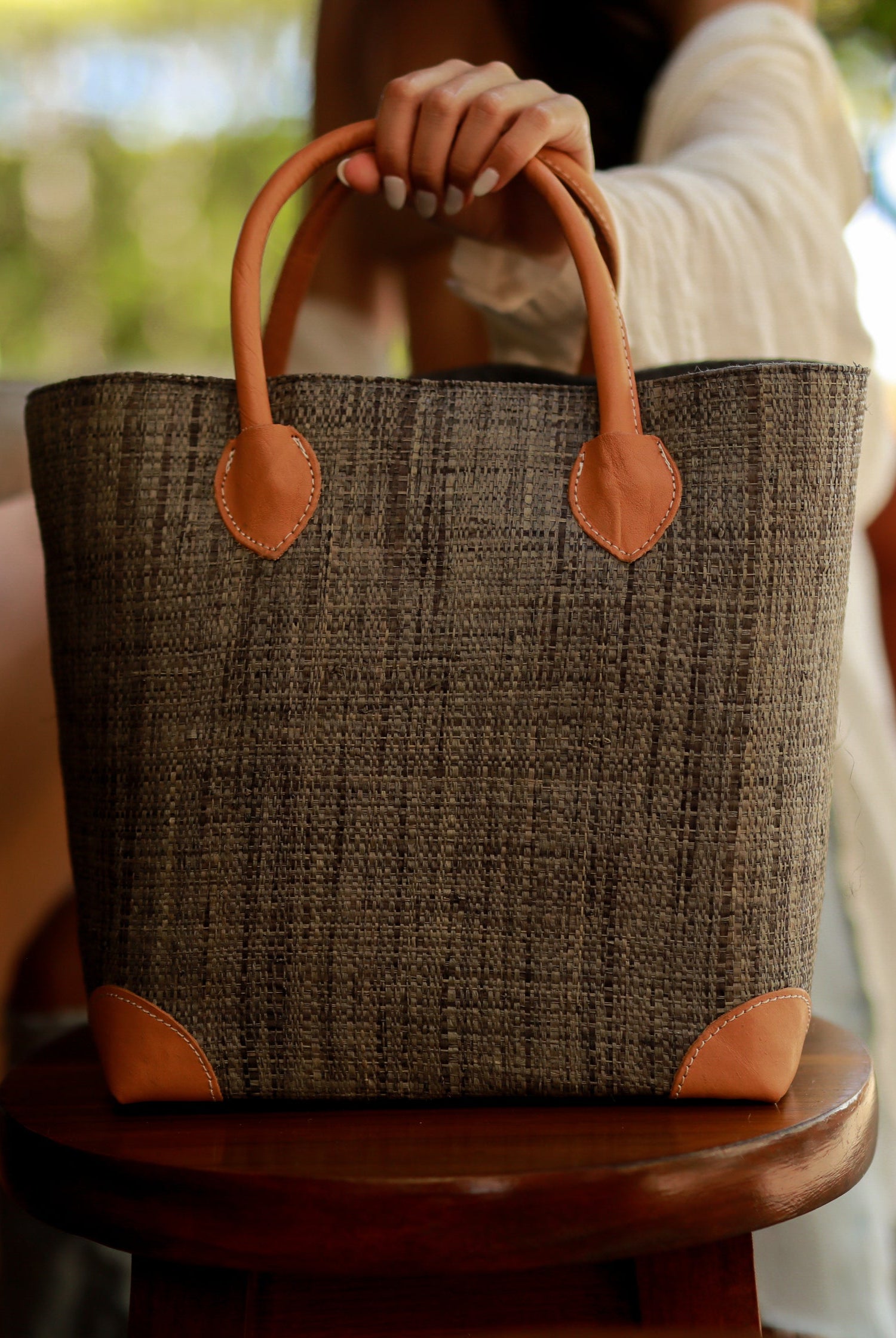 Model wearing Augustine Straw Basket Bag handmade loomed raffia handbag with leather corners and handles in grey - Shebobo
