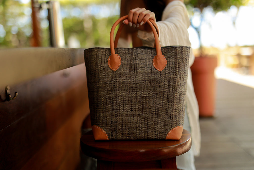 Model wearing Augustine Straw Basket Bag handmade loomed raffia handbag with leather corners and handles in grey - Shebobo