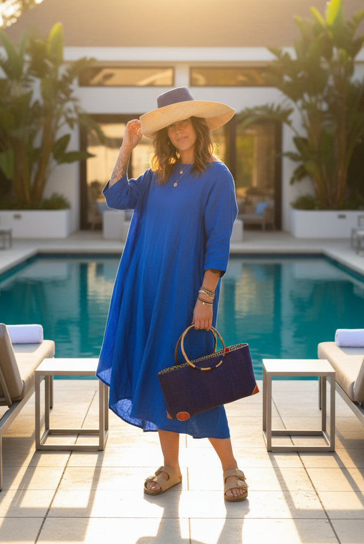 Model wearing Bebe Straw Handbag with Bamboo Handle handmade loomed natural raffia palm fiber in a solid hue of Dusk dark/navy/blue with molded circular bamboo handles, leather feet, and assorted print African wax-cloth fabric liner - Shebobo (with Monica 5" & 7" Wide Brim Two Tone Packable Straw Sun Hats)