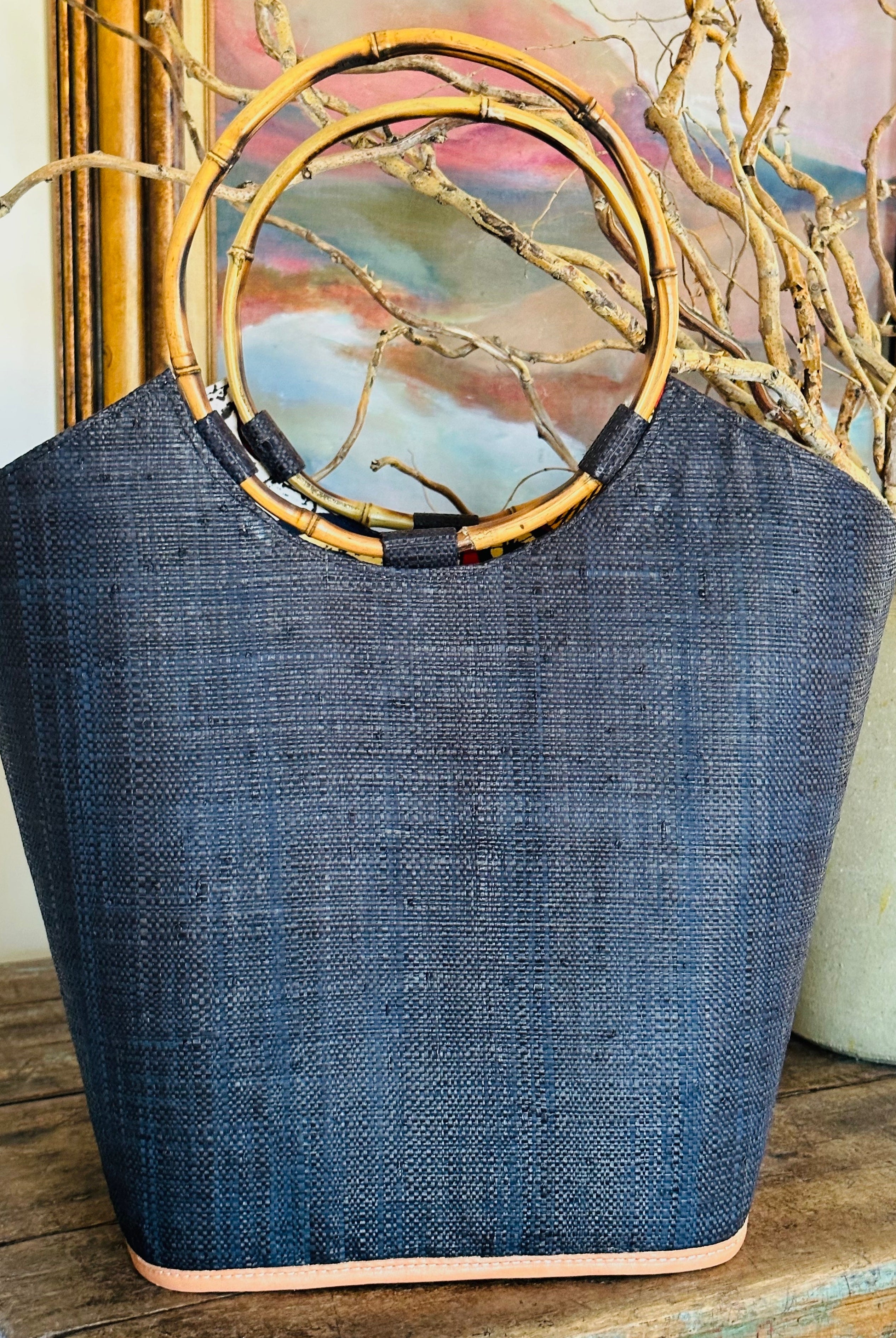 Lifestyle shot of Carmen Straw Bucket Bag Black Handmade Loomed Raffia with assorted African Print Liner, Bamboo Handles, and leather binding - Shebobo