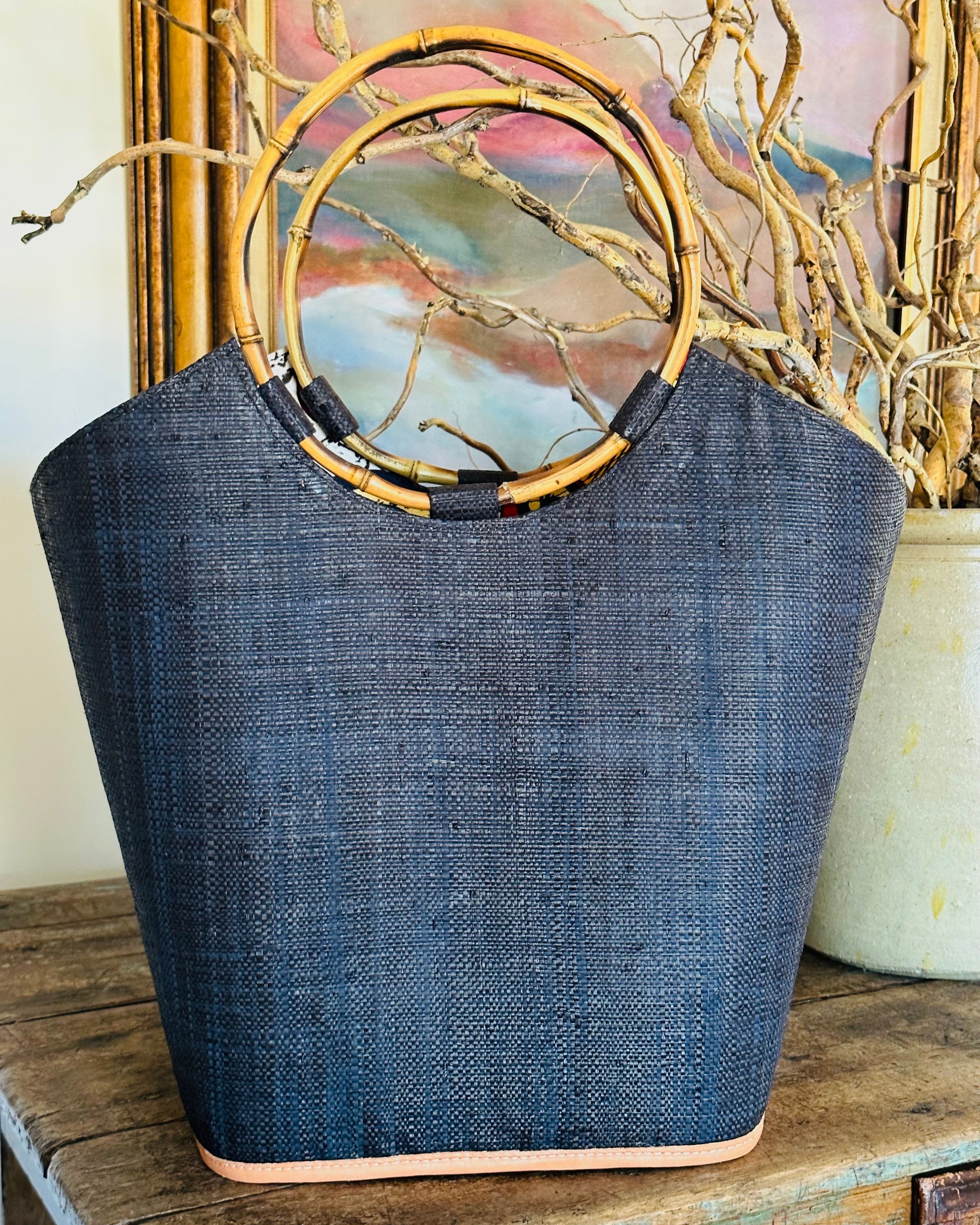 Lifestyle shot of Carmen Straw Bucket Bag Black Handmade Loomed Raffia with assorted African Print Liner, Bamboo Handles, and leather binding - Shebobo