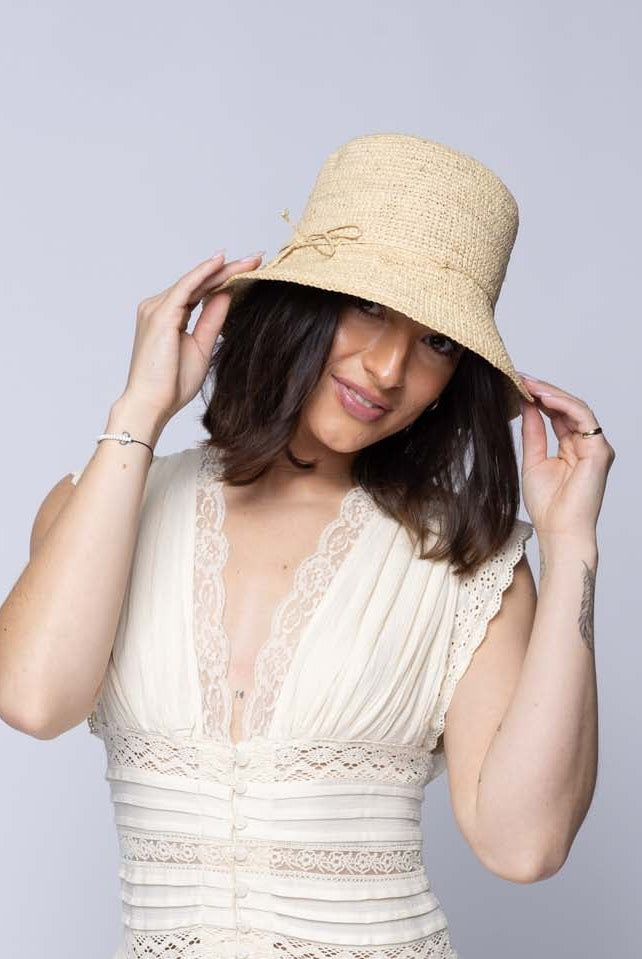 Model wearing Bobbi 3" Brim Crochet Bucket Raffia Straw Hats handmade natural raffia palm fiber in a subtle crochet link texture spiraling out from the top crown of the hat to the edge of the brim in a solid hue of natural straw color with matching braided adjustable hat band sun hat - Shebobo
