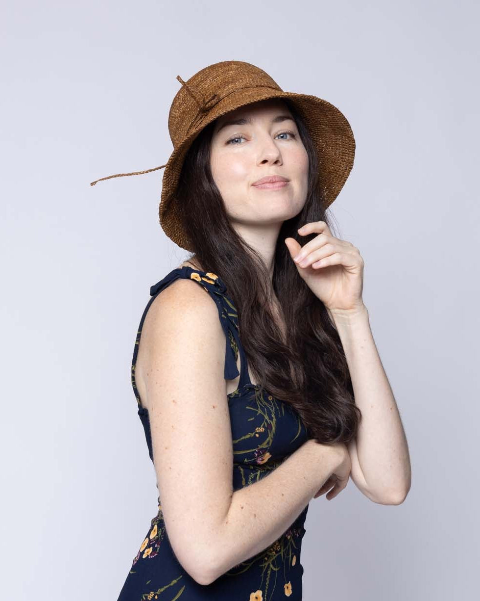 Model wearing Bobbi 3" Brim Crochet Bucket Raffia Straw Hats handmade natural raffia palm fiber in a subtle crochet link texture spiraling out from the top crown of the hat to the edge of the brim in a solid hue of tobacco dark/cinnamon brown with matching braided adjustable hat band sun hat - Shebobo