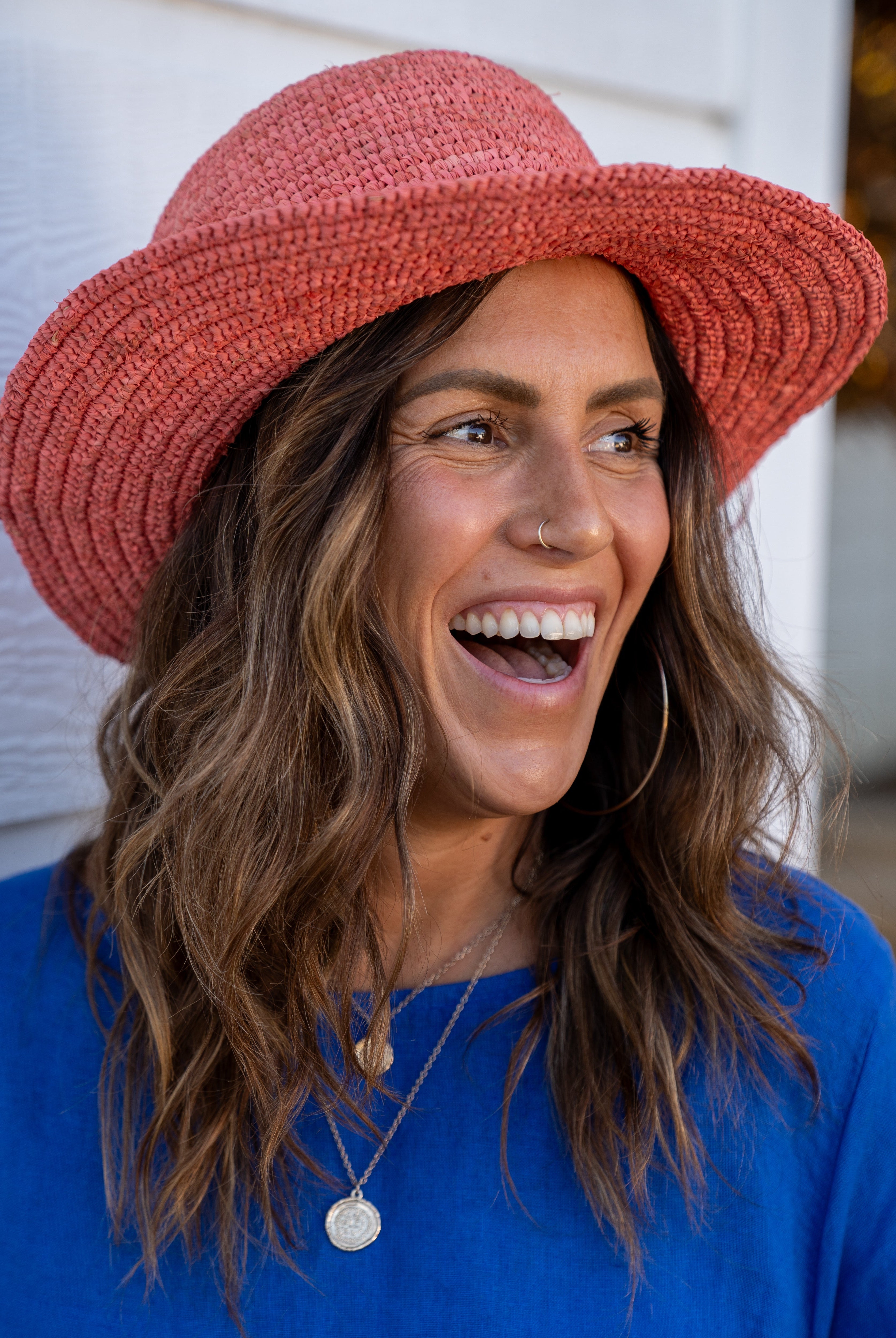 Model wearing 3" Brim Bolero Crochet Straw Sun Hats handmade crochet natural raffia palm fiber in a solid hue of Cherry Blossom pink/orange making a concentric pattern from the center top of the flattened crown spiraling out to the edge of the brim with matching adjustable raffia braid hat band - Shebobo