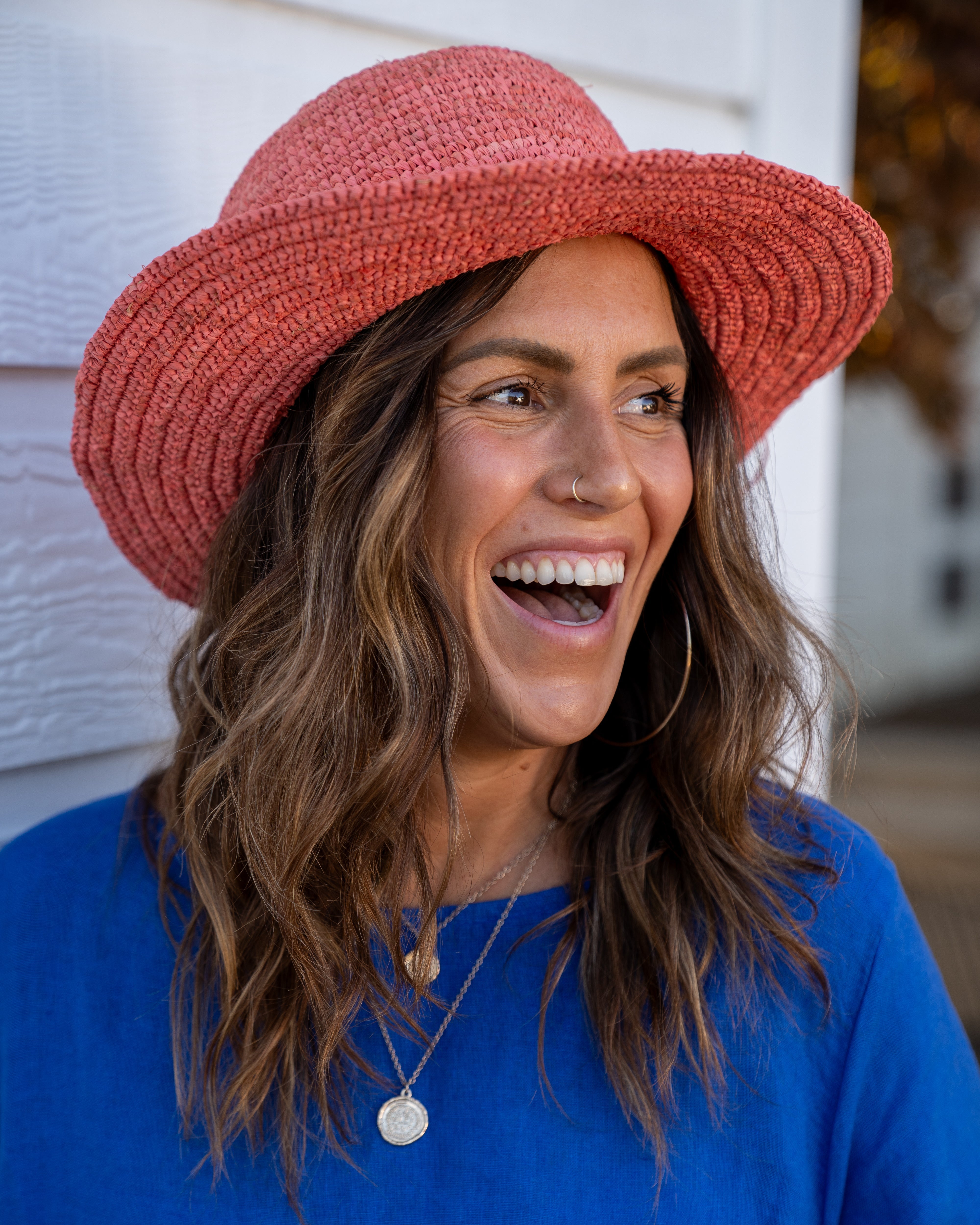 Model wearing 3" Brim Bolero Crochet Straw Sun Hats handmade crochet natural raffia palm fiber in a solid hue of Cherry Blossom pink/orange making a concentric pattern from the center top of the flattened crown spiraling out to the edge of the brim with matching adjustable raffia braid hat band - Shebobo