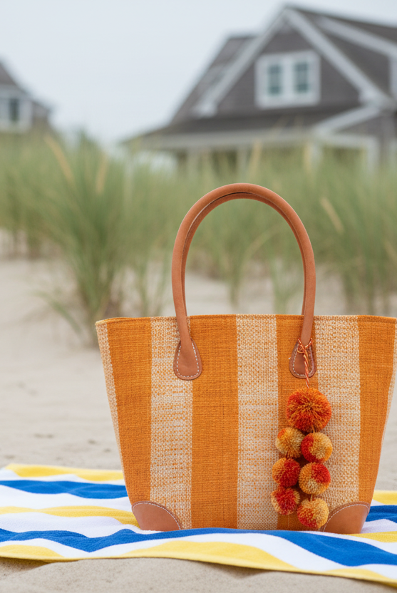 Lifestyle view Bora Bora Saffron Two Tone Stripes Straw Basket Bag with Waterfall Pompoms Charm Embellishment handmade loomed natural raffia palm fiber in a multicolor horizontal stripe pattern of even width wide bands of saffron orange/yellow and natural straw color with leather handles and feet plus matching waterfall pompom charm embellishment handbag beach bag - Shebobo