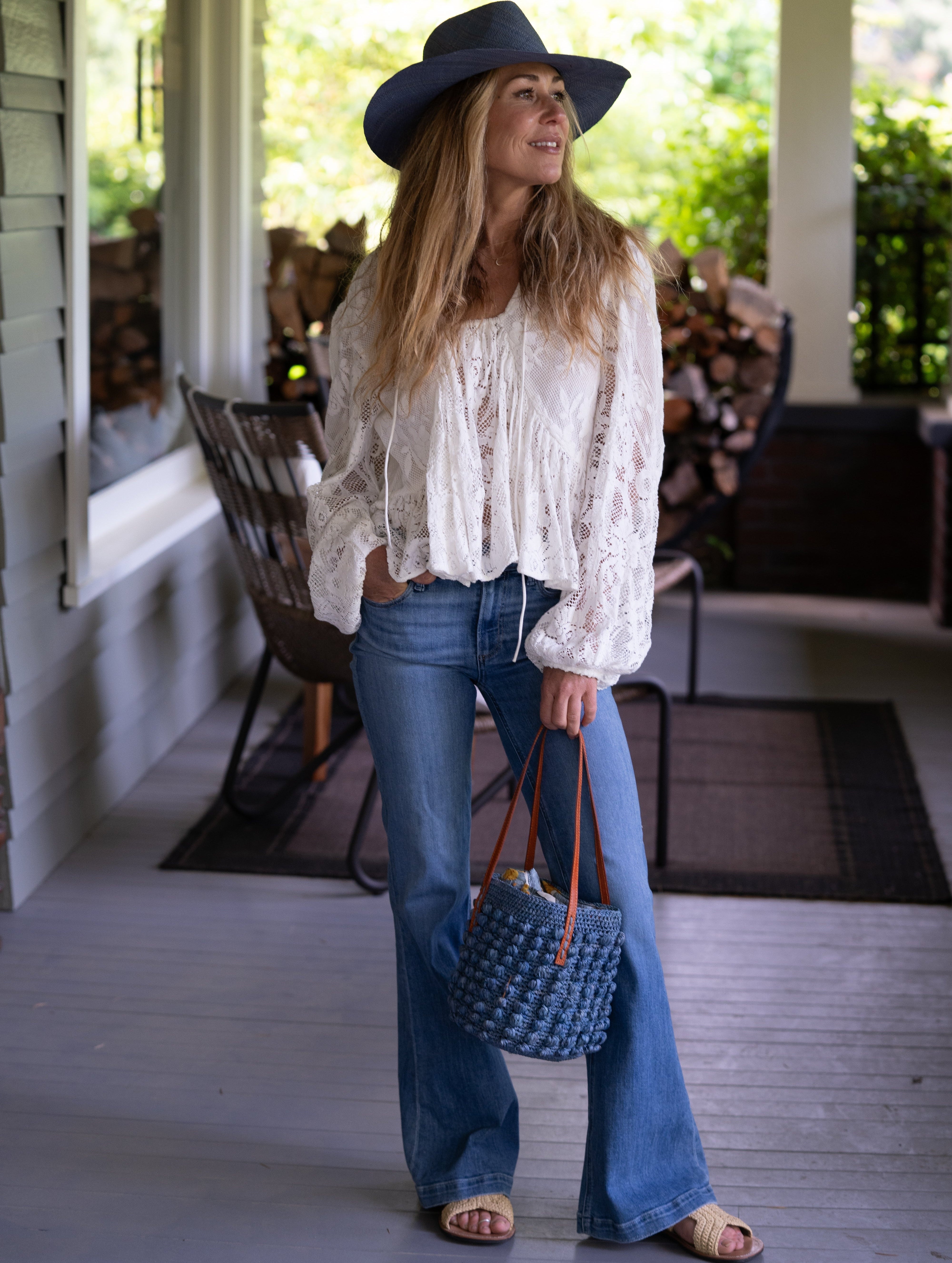 Model wearing Boucle Denim Crochet Small Straw Handbag handmade woven raffia palm fiber in a solid hue of denim retro/light/blue in a supple nub/ball texture of horizontal bands around the bag with link weave around the top plus assorted print drawstring liner and leather handles shoulder bag purse - Shebobo (with Panama Unisex Straw Hats)