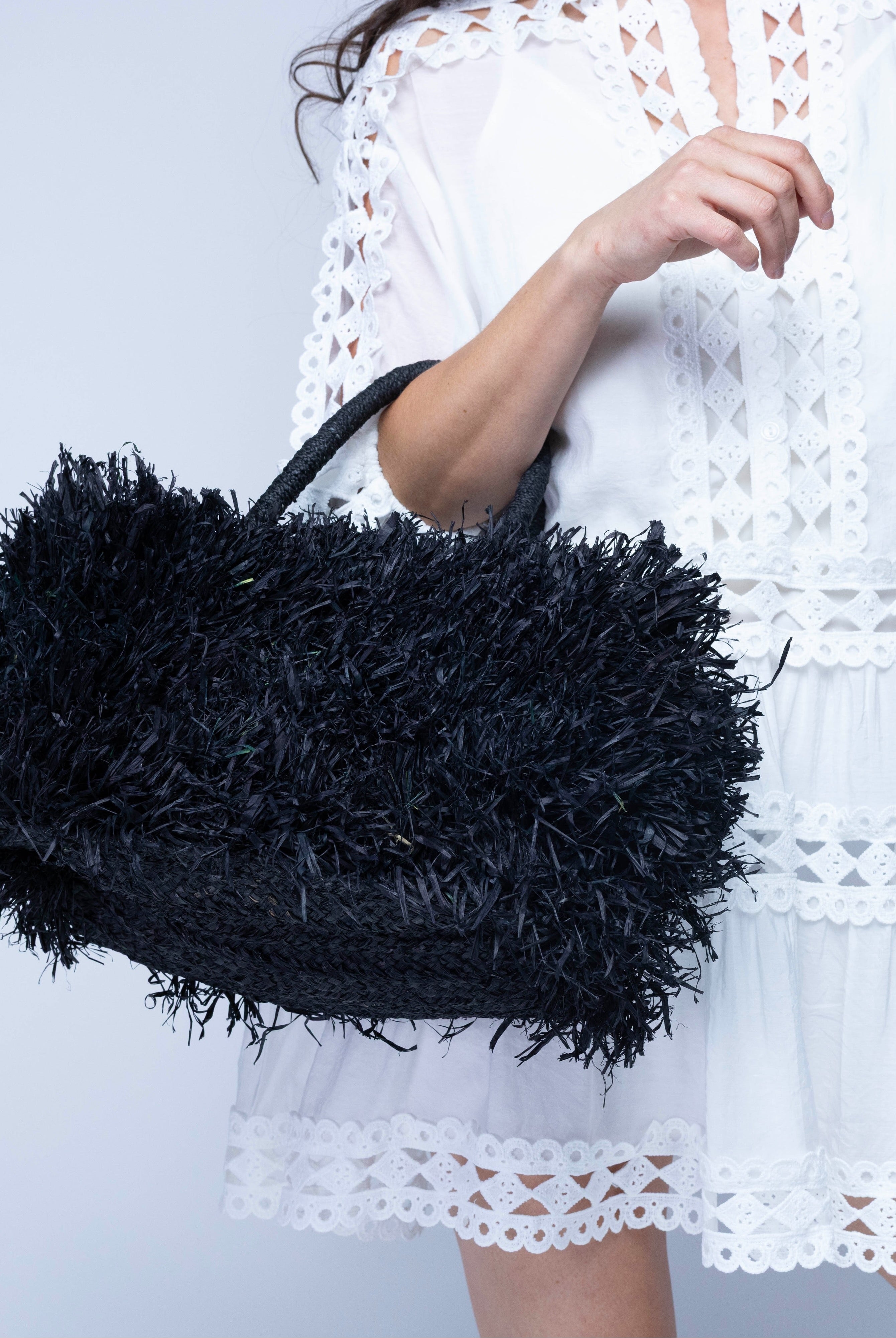 Model wearing Calypso Pompom Pouf Crochet Straw Basket Handbag handmade natural raffia palm fiber in a solid hue of Black with brushed fringe strands crochet and knotted into a pouf texture with matching wrapped handles purse - Shebobo