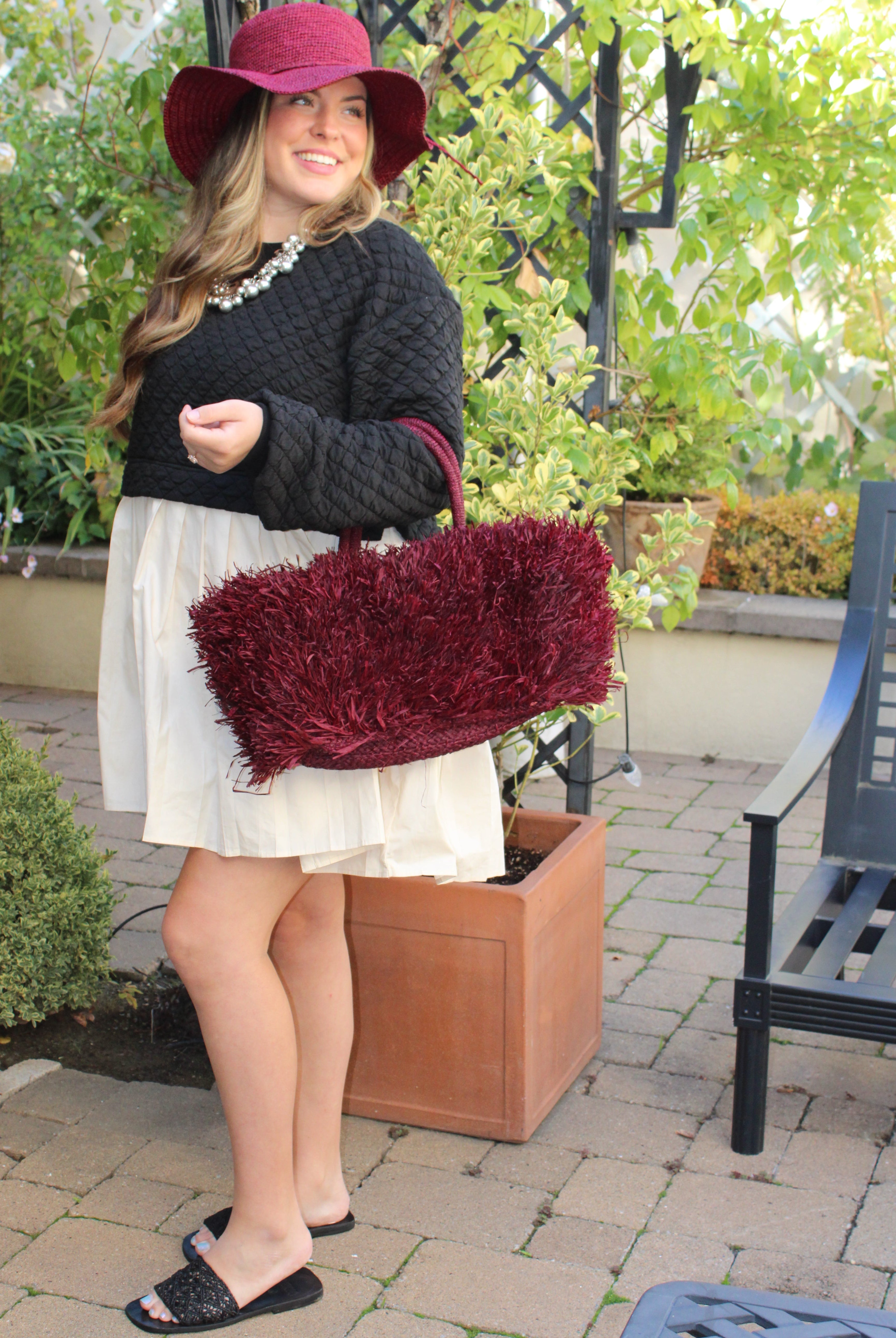 Model wearing Calypso Pompom Pouf Crochet Straw Basket Handbag handmade natural raffia palm fiber in a solid hue of Umberwine burgunday/bordeaux/dark/purple/red with brushed fringe strands crochet and knotted into a pouf texture with matching wrapped handles purse - Shebobo (with Bolero 3" Brim Crochet Straw Sun Hats)
