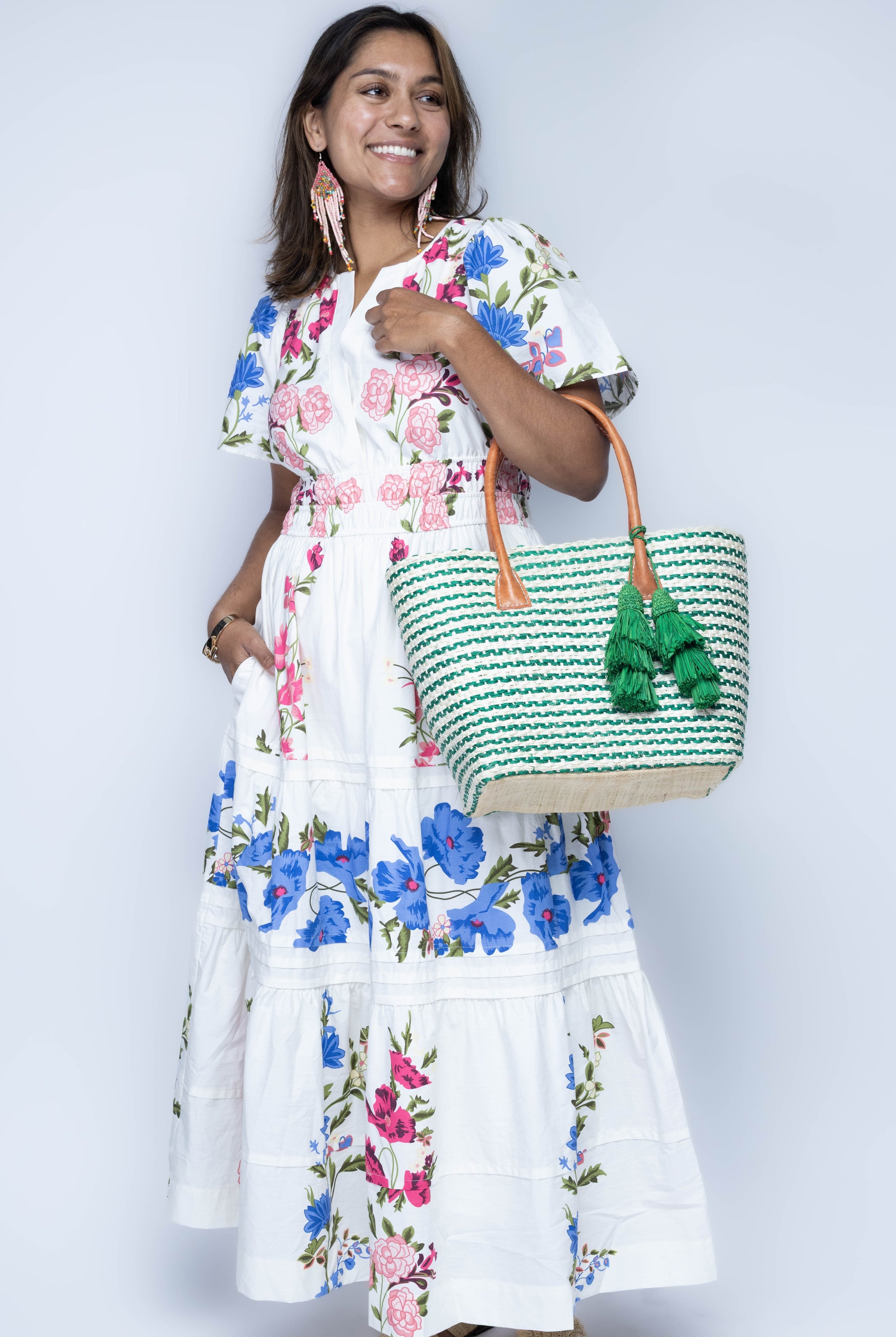 Model wearing Cancun Small Sisal Basket Bag with Tassel Charm handmade natural sisal fibers woven into even width horizontal bands of deep green and natural straw color that create a pinstripe pattern with matching knotted raffia tufts tassel charm embellishment and leather handles beach bag - Shebobo