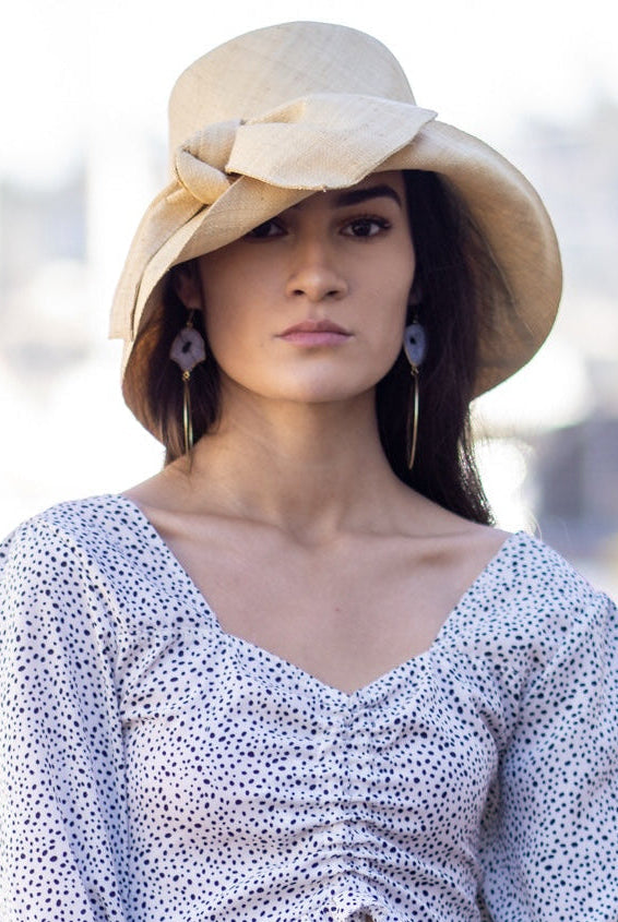 Model wearing Cara Natural straw color big bow embellishment handmade loomed raffia straw bucket style cloche sun hat - Shebobo