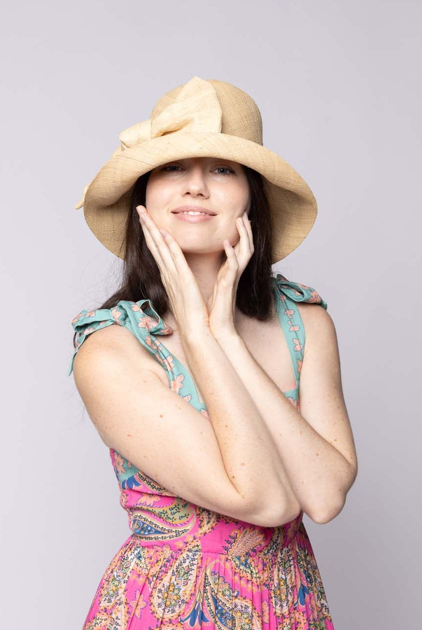 Model wearing Cara Natural straw color big bow embellishment handmade loomed raffia straw bucket style cloche sun hat with matching oversized bow - Shebobo